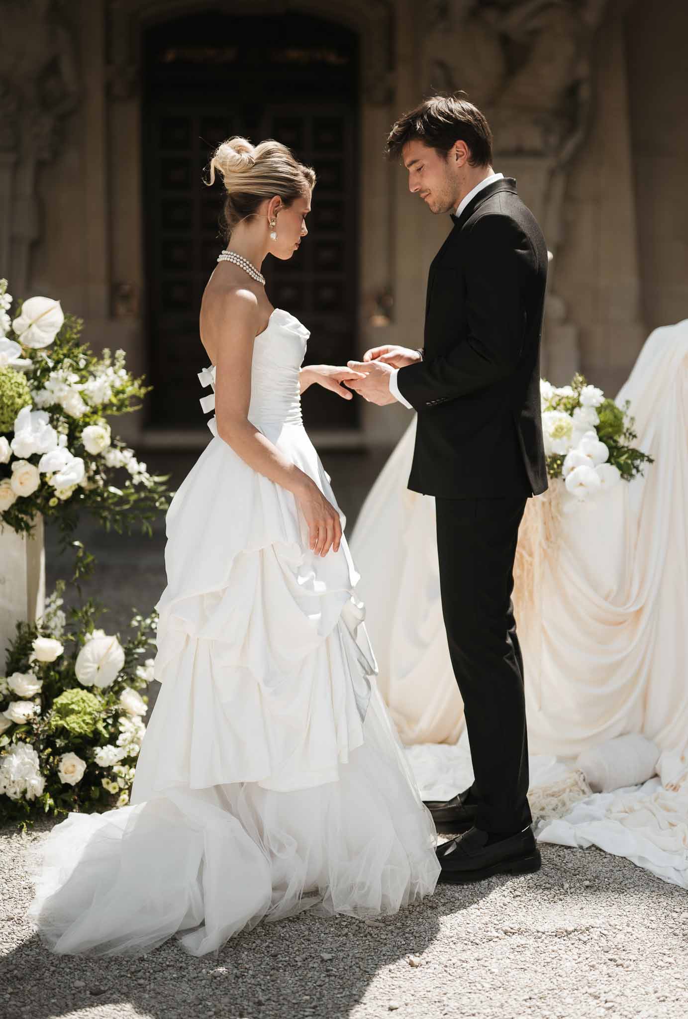 Ring exchange at stone building altar with white rose urns and champagne fabric drape in sunlight