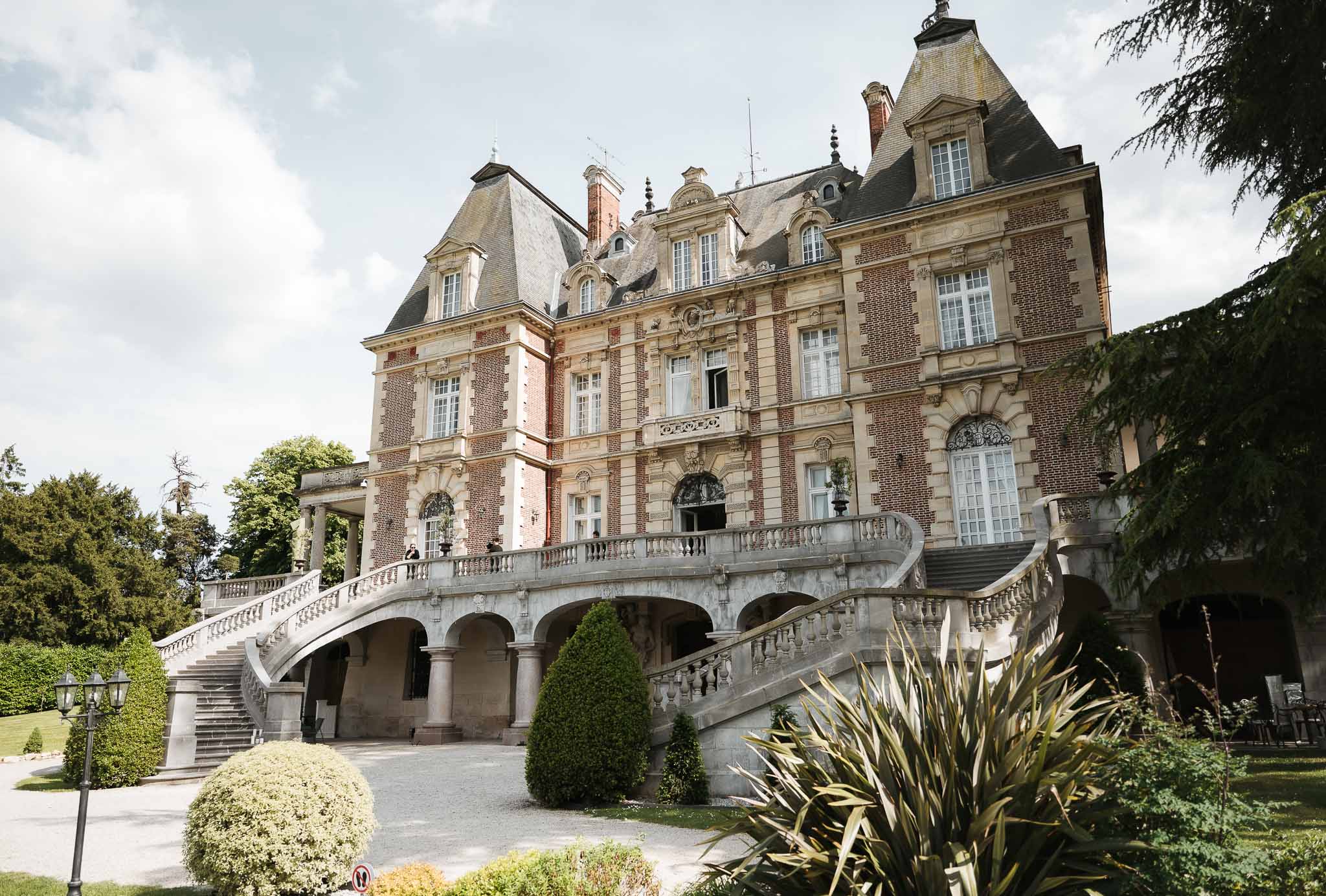Second Empire chateau with red brick, mansard roofs, and horseshoe staircase framed by boxwood hedges