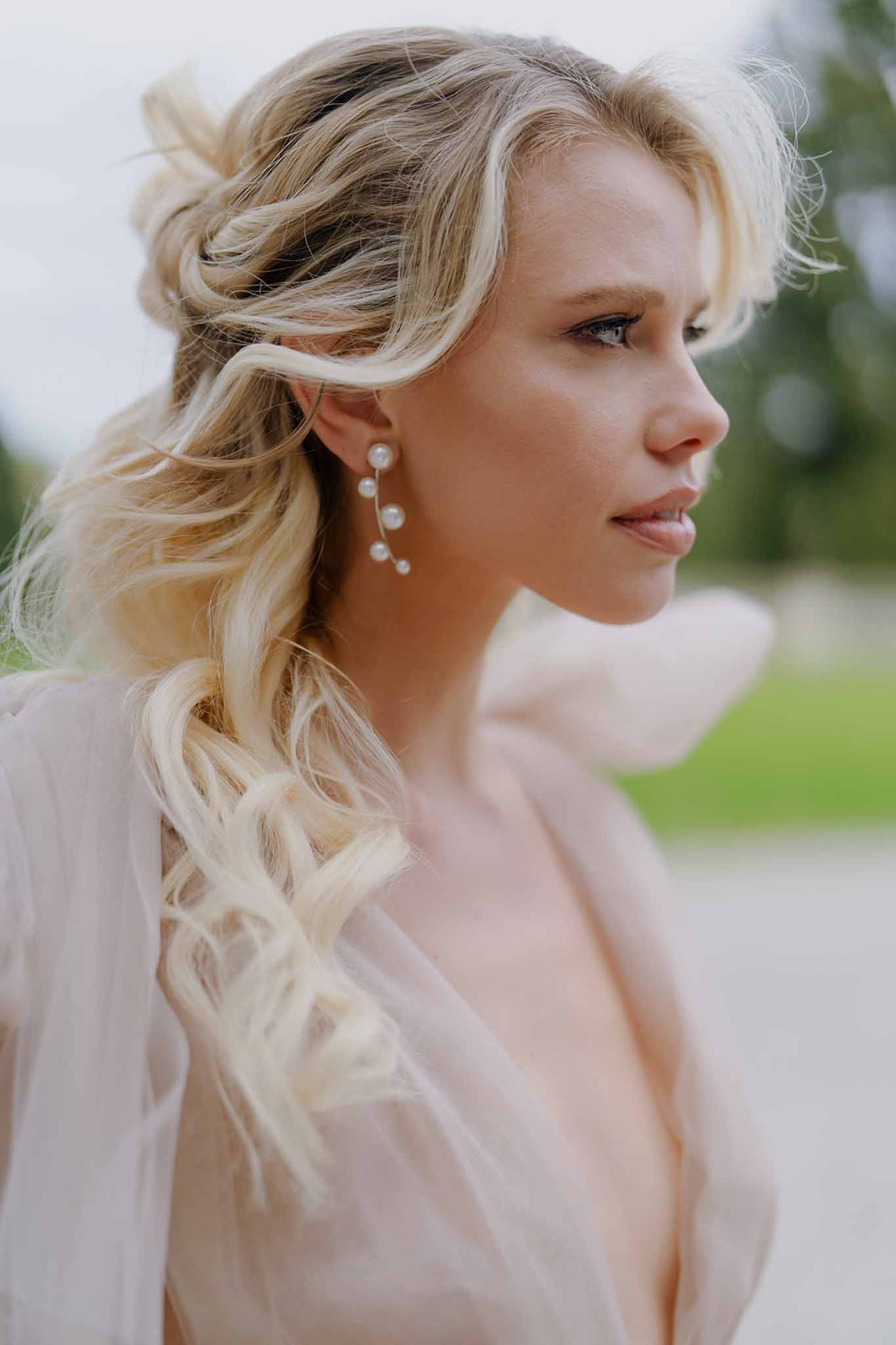 Close-up portrait of bride in blush pink robe with pearl drop earrings and loose wavy blonde hair