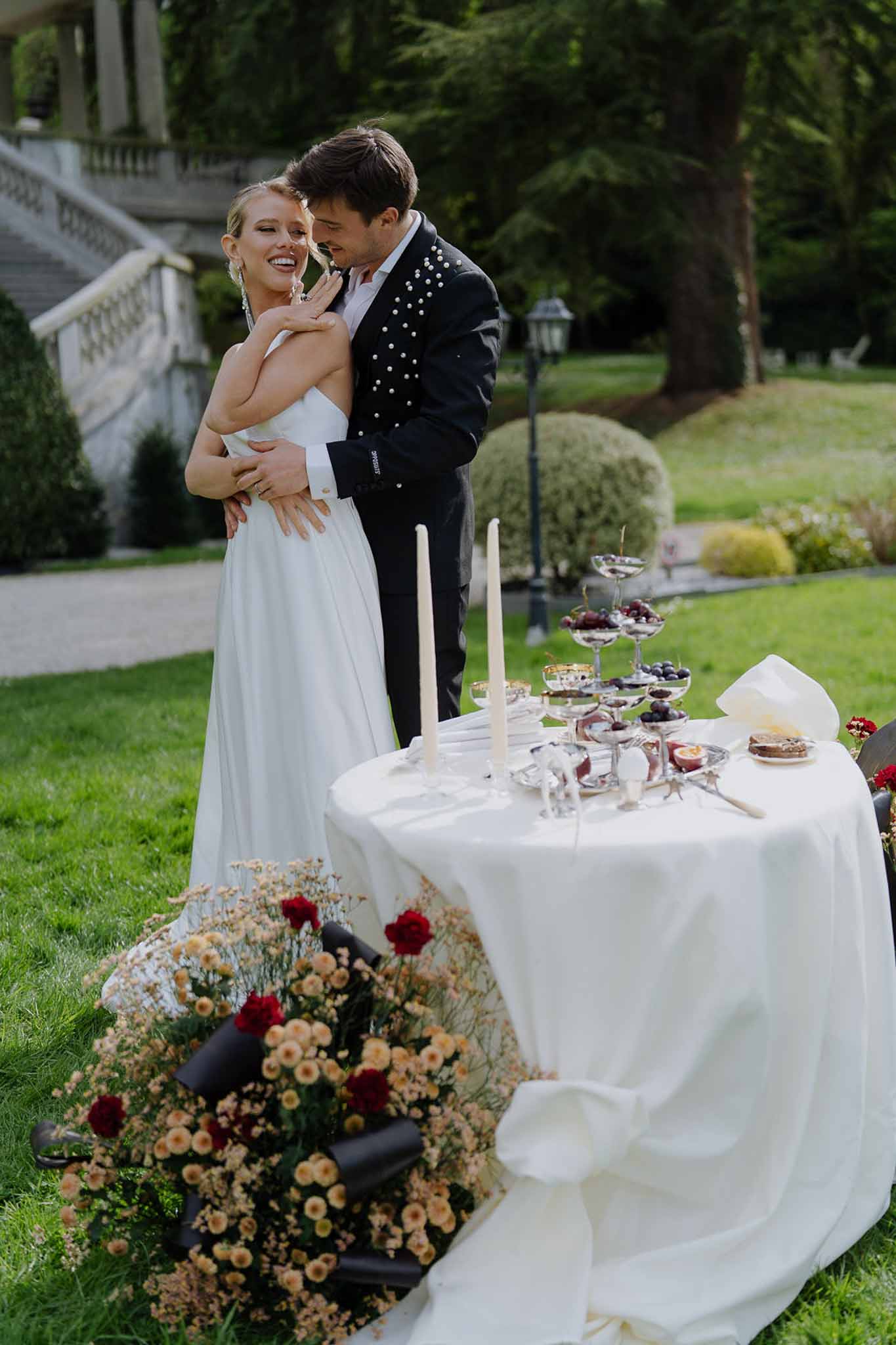 Groom nuzzling laughing bride beside sweetheart table with amber chrysanthemums and berry desserts