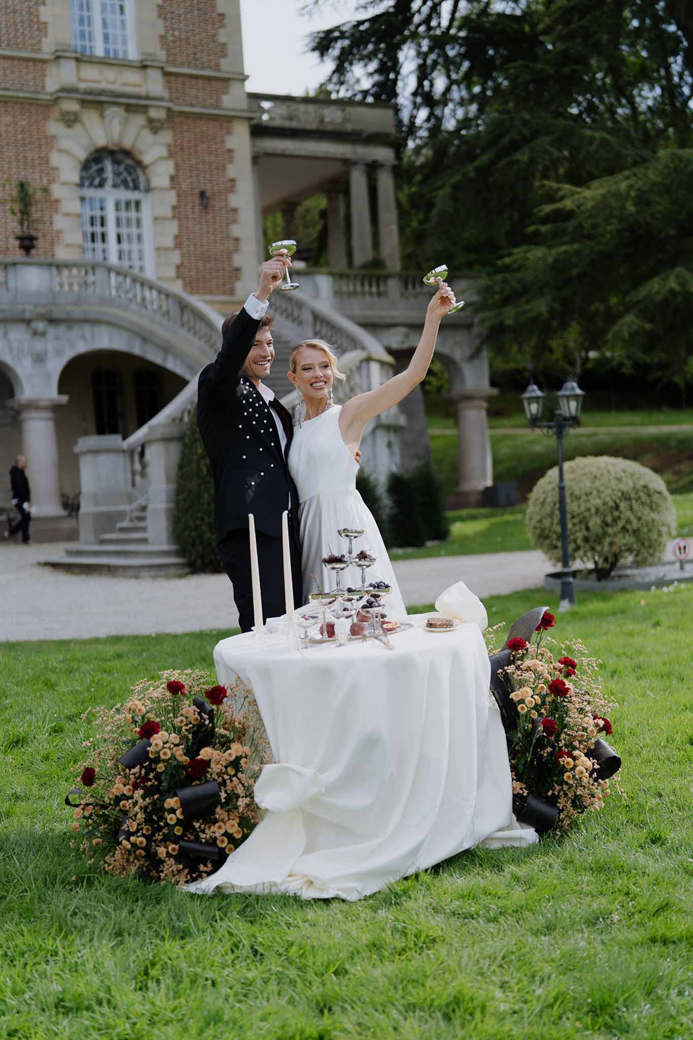 Bride and groom toasting with champagne tower at sweetheart table before grand chateau staircase