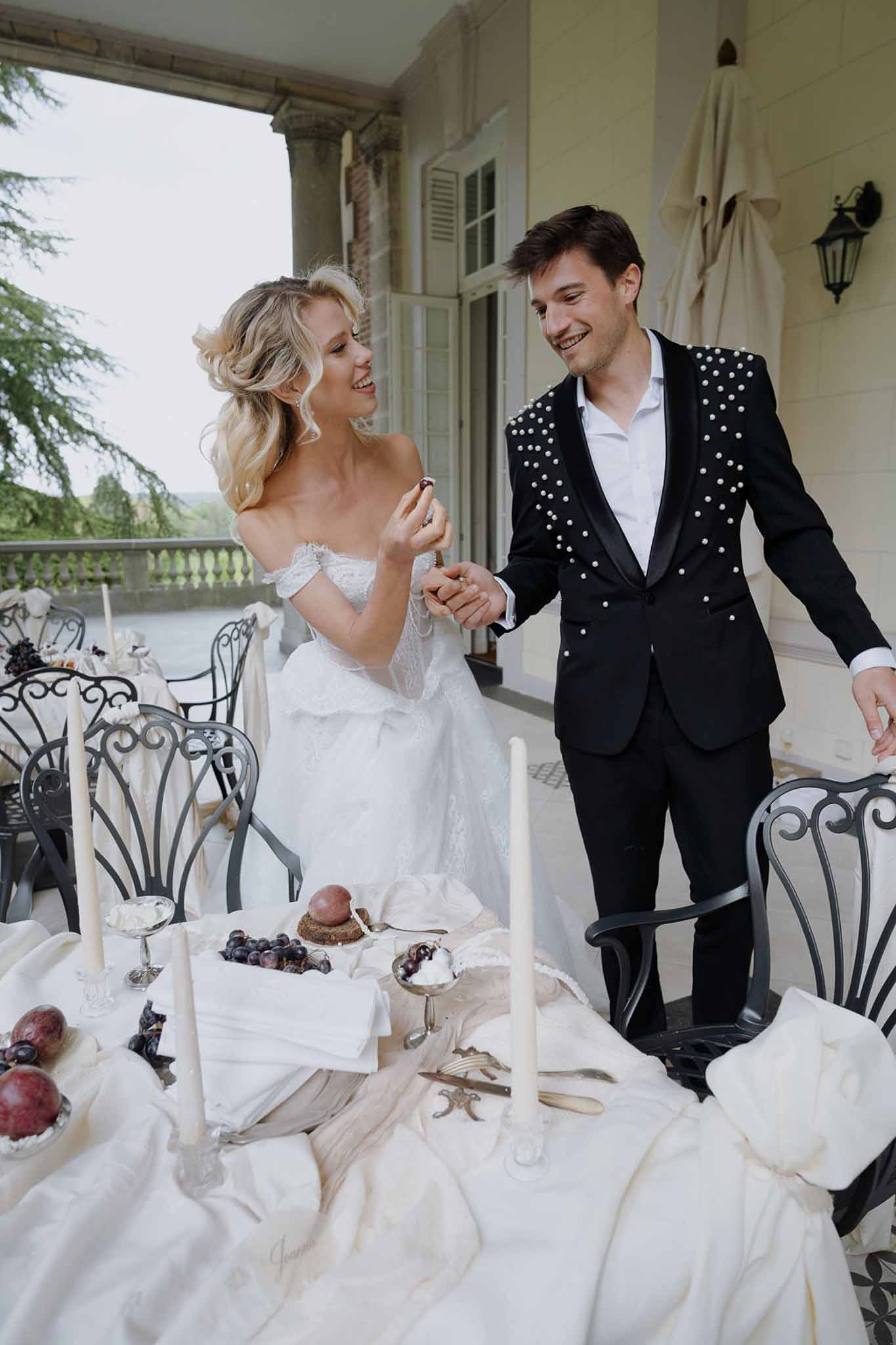 Bride and groom share a playful moment beside a styled tablescape on a chateau terrace