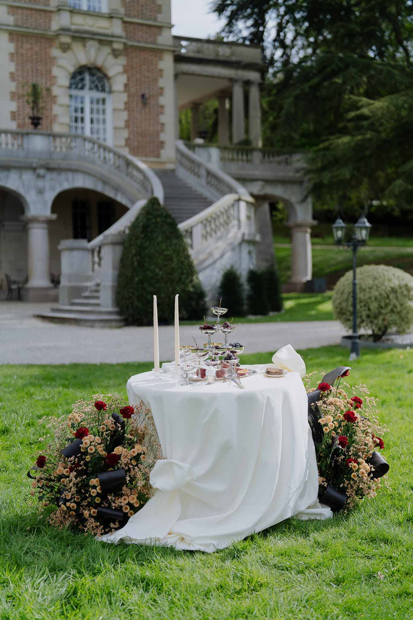 Sweetheart table with champagne coupe tower and amber chrysanthemum floor arrangements before chateau double staircase