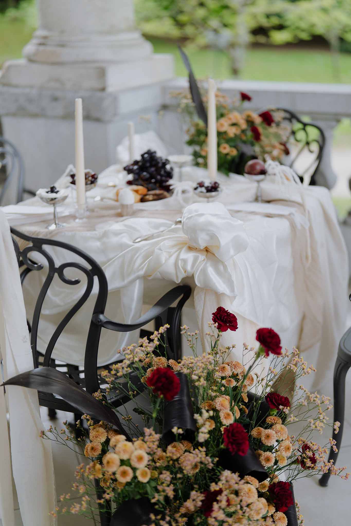 Styled sweetheart table with ivory draping, tall taper candles, dark fruits, and burgundy and peach floral arrangement on ...