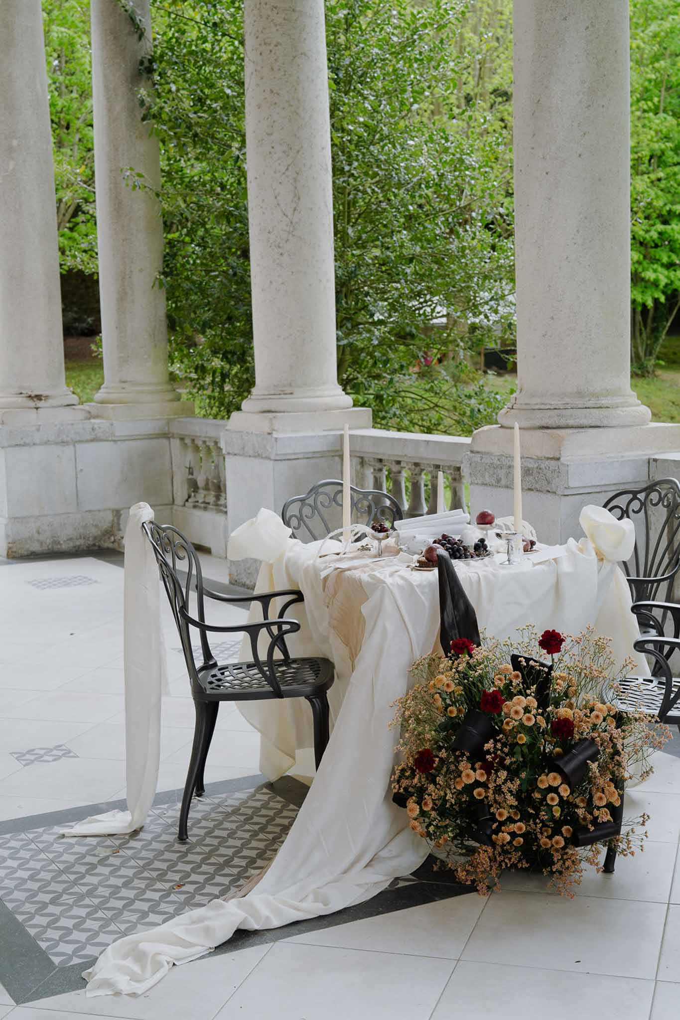 Sweetheart table with black runner and amber chrysanthemum arrangement on columned terrace with geometric tile floor