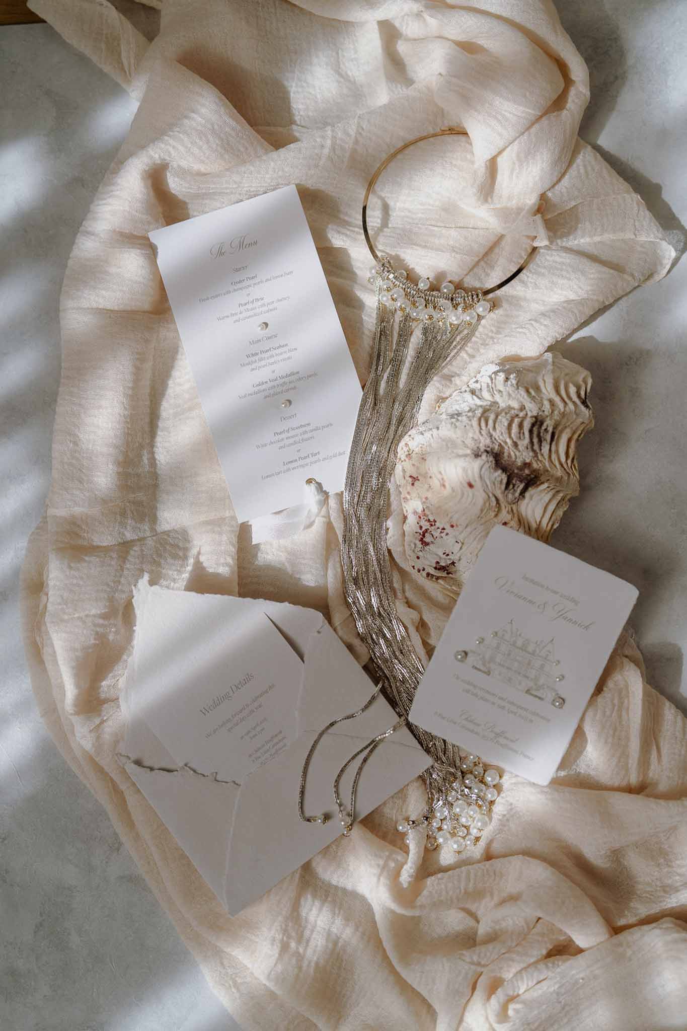 Stationery flat lay with venue illustration pearl embellishments gold tiara and oyster shell on silk