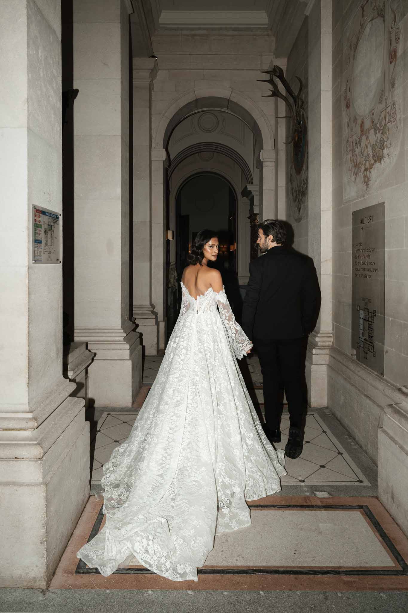 Bride and groom walking through classical stone corridor at elegant indoor venue