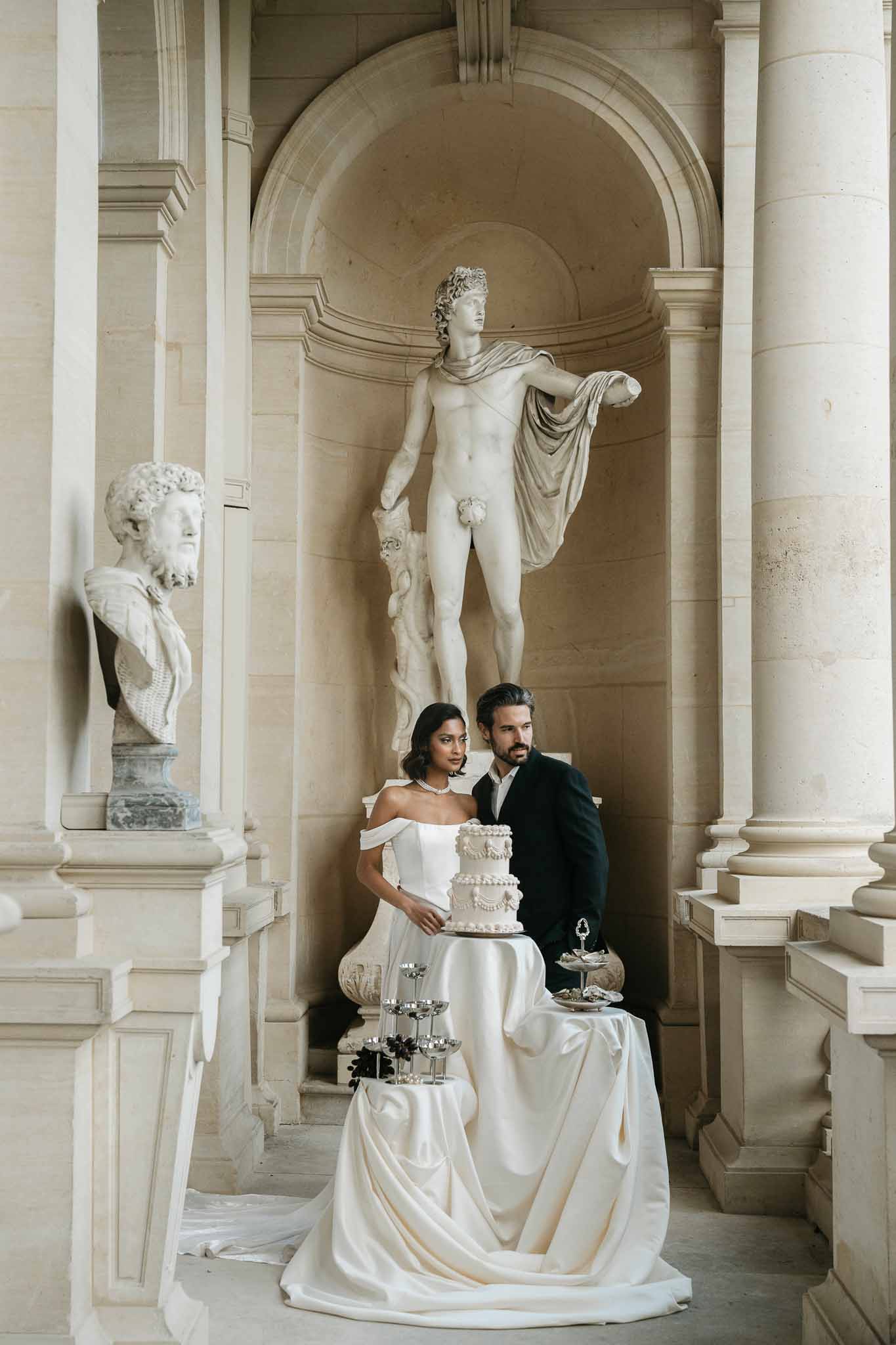 Bride and groom portrait with wedding cake in classical stone gallery with marble columns and statuary