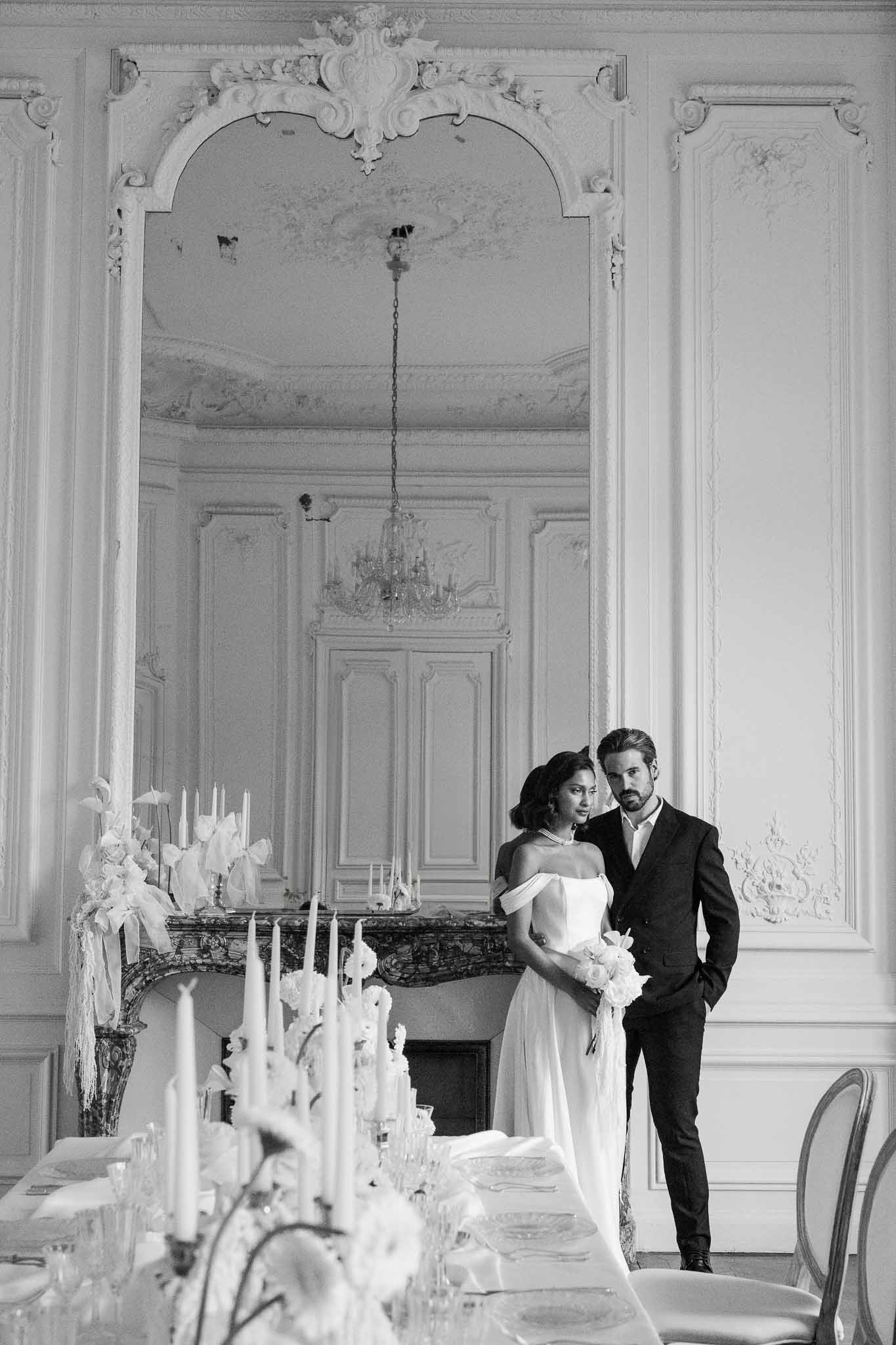 Bride and groom portrait in elegant neoclassical ballroom with crystal chandelier and formal dining setup