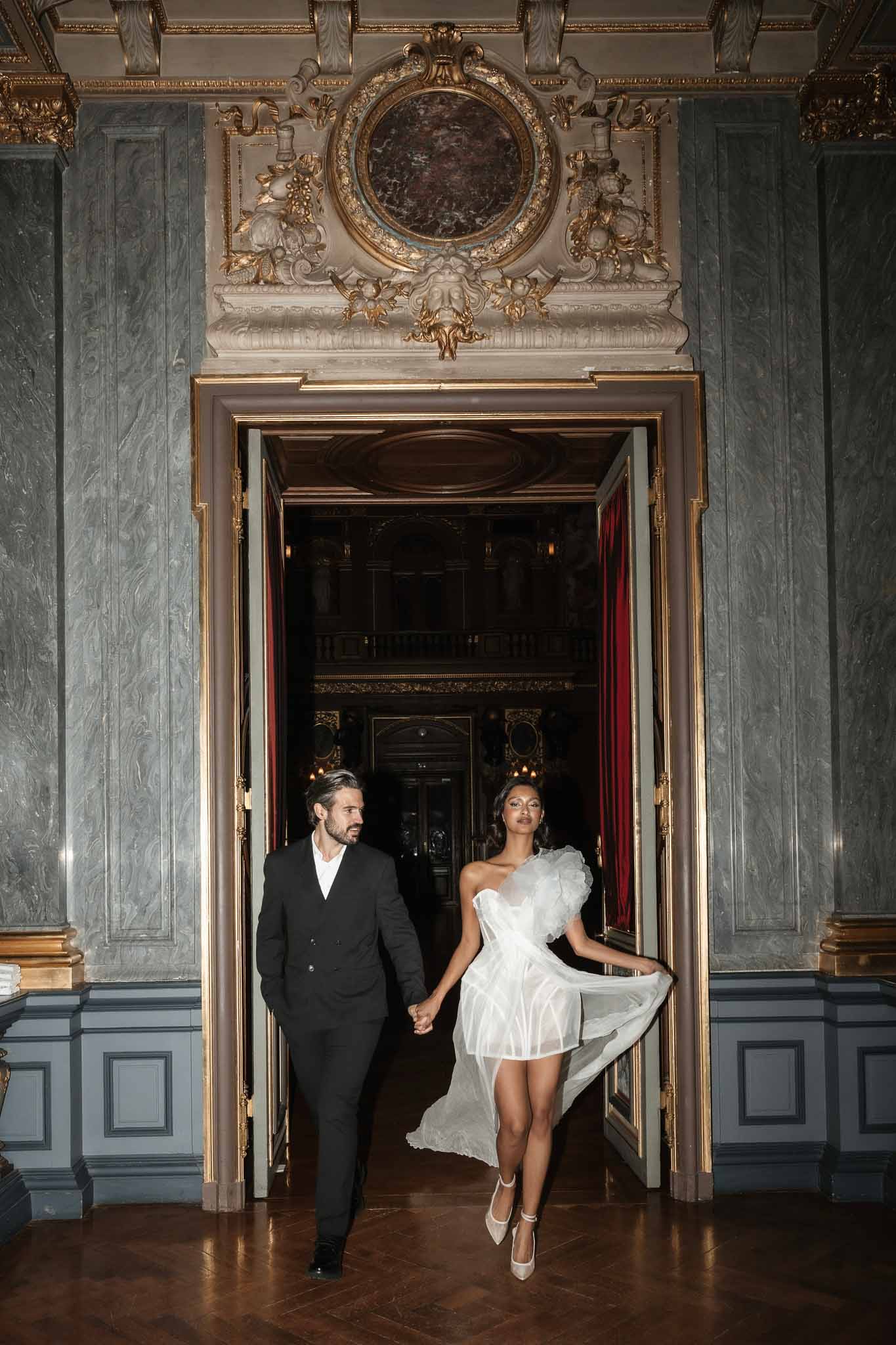 Bride and groom walking through ornate doorway in grand classical interior with marble walls and gilded details