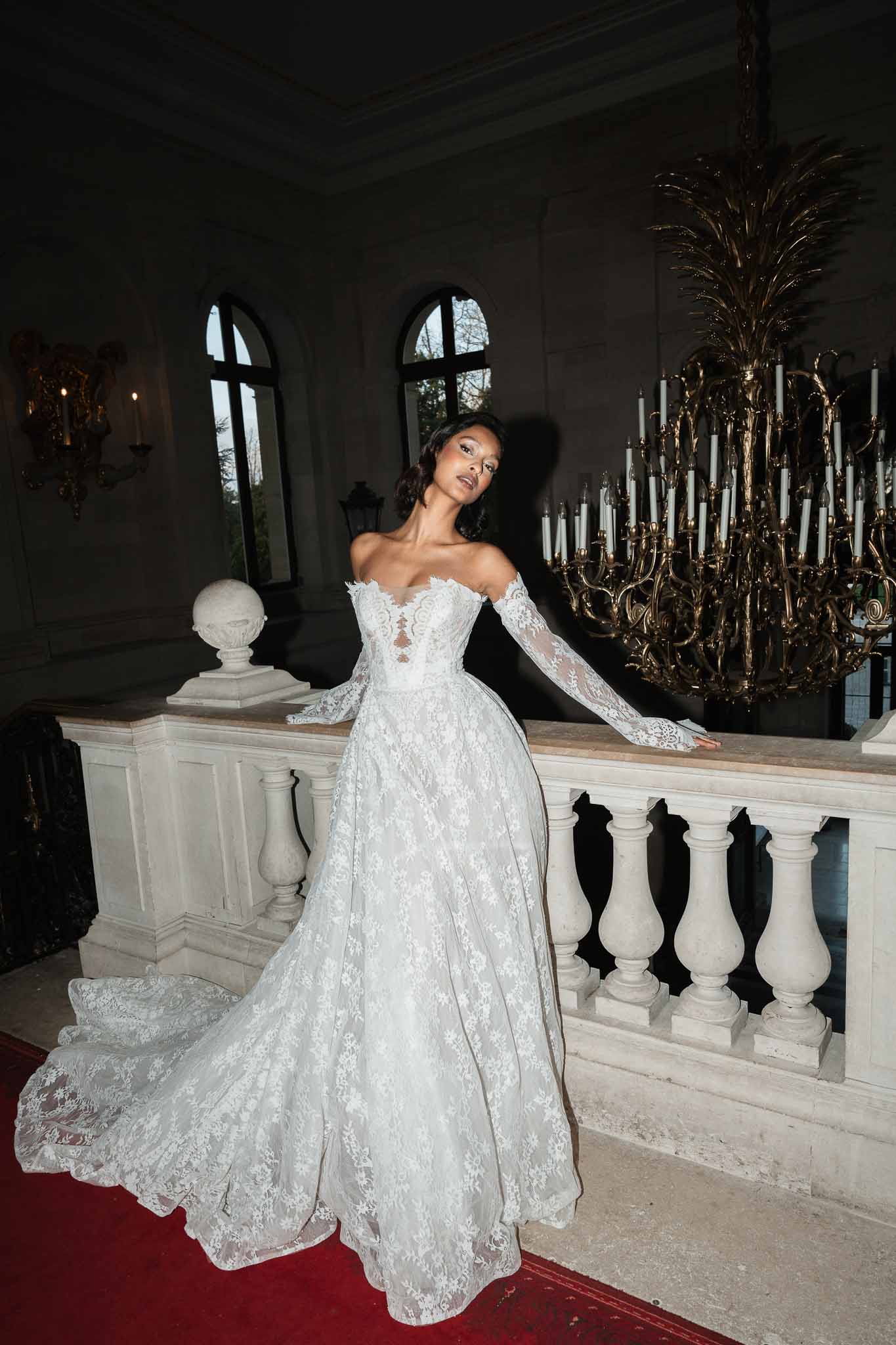 Bride in ivory lace gown posing in grand ballroom with classical architecture and candelabra