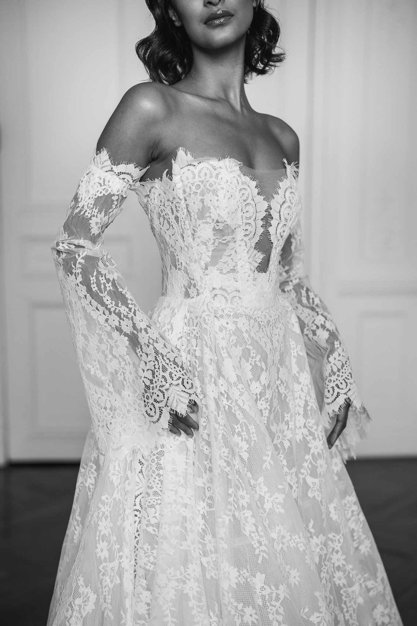 Bride in intricate lace off-shoulder wedding dress, black and white portrait showcasing dress craftsmanship
