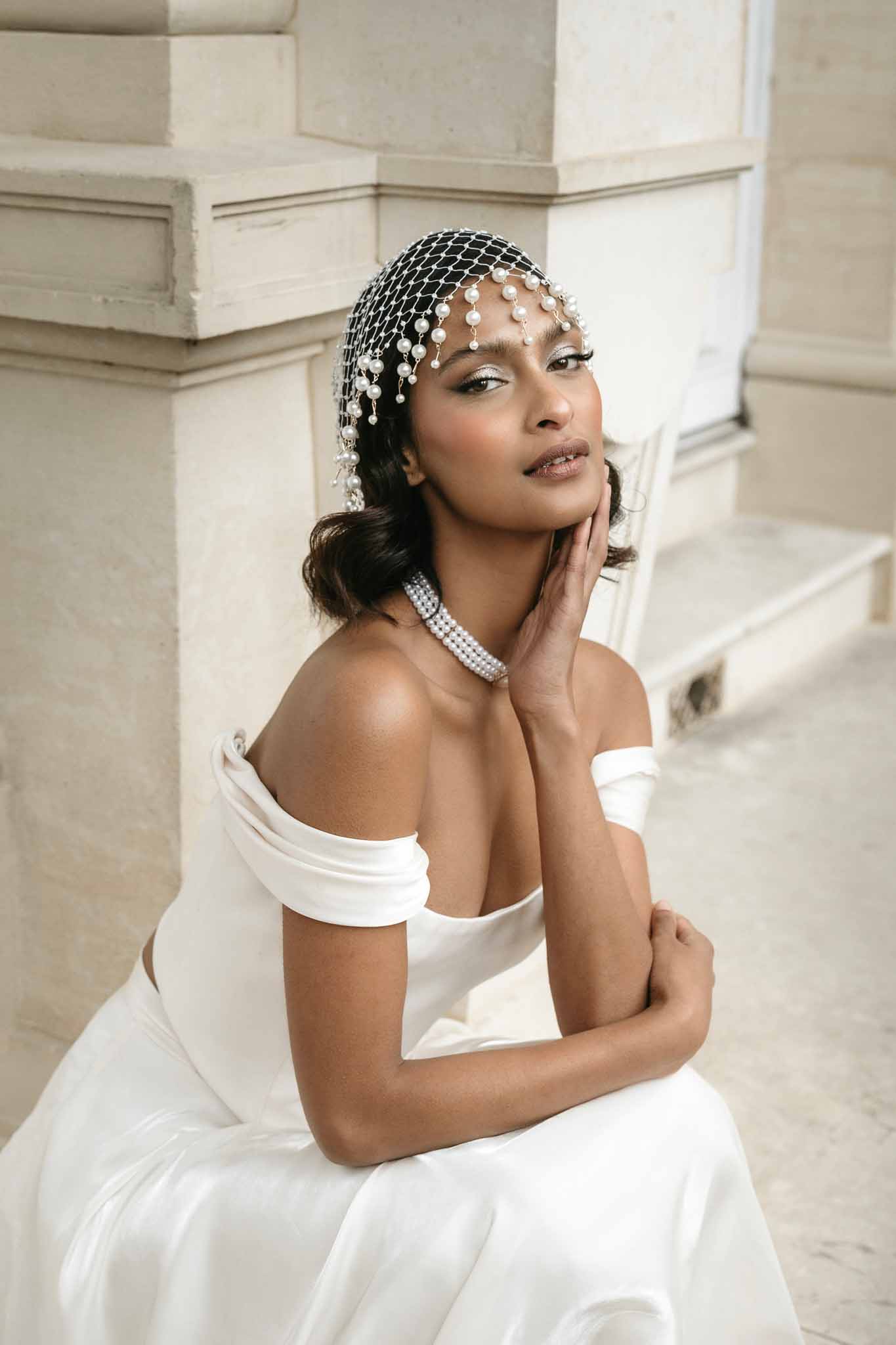 Bride in off-shoulder dress with pearl-embellished black veil against stone architecture background