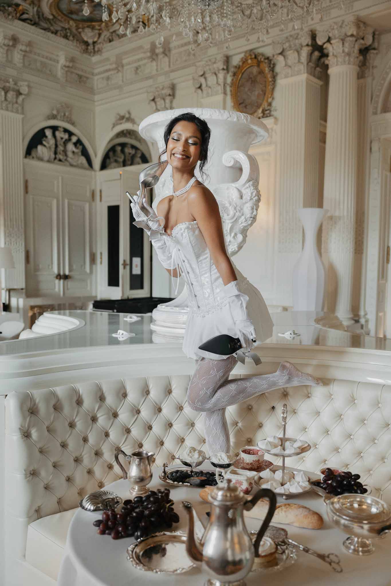 Bride in white corset dress poses in neoclassical interior with crystal chandelier and formal table setting