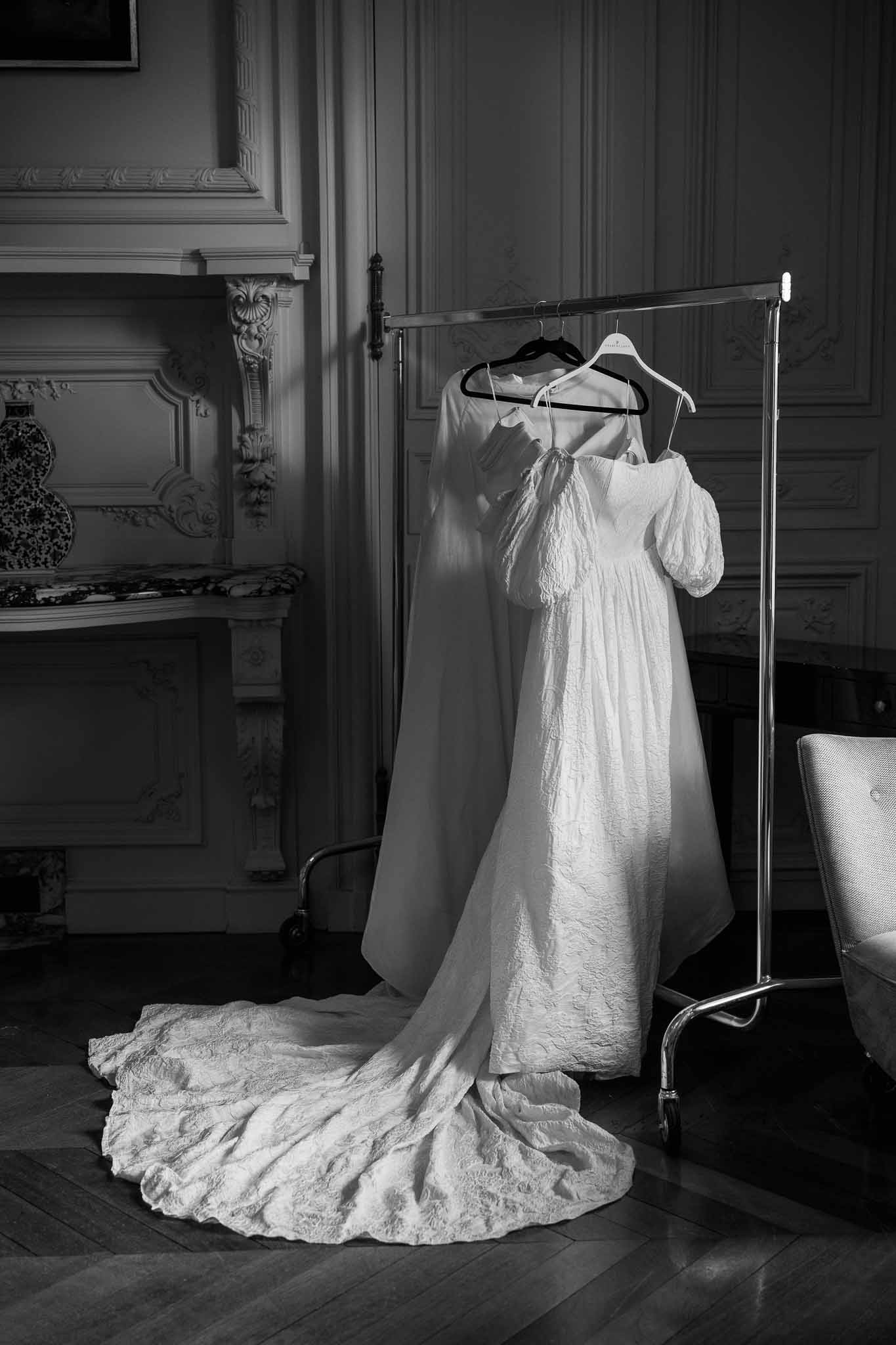 Wedding dress hanging on rack in ornate room with fireplace mantel