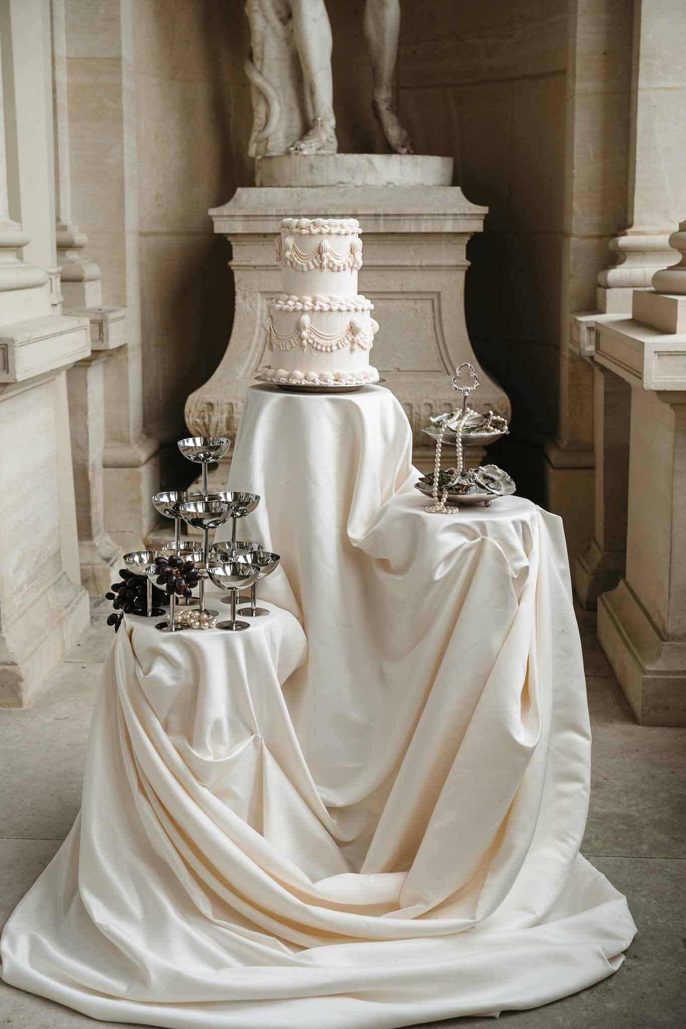 Tiered wedding cake display with champagne tower in classical stone corridor with columns