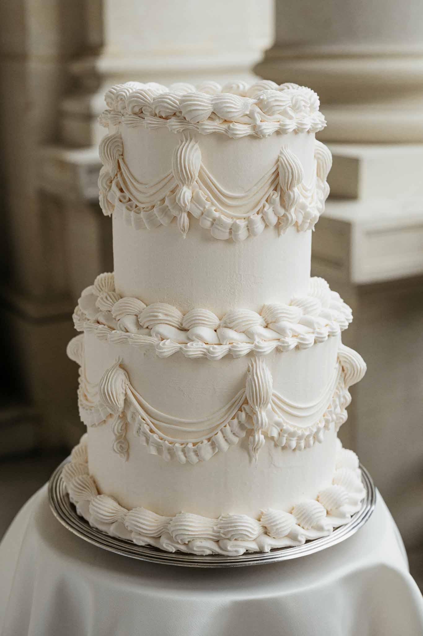 Three-tiered ivory wedding cake with ornate piped detailing at formal reception venue