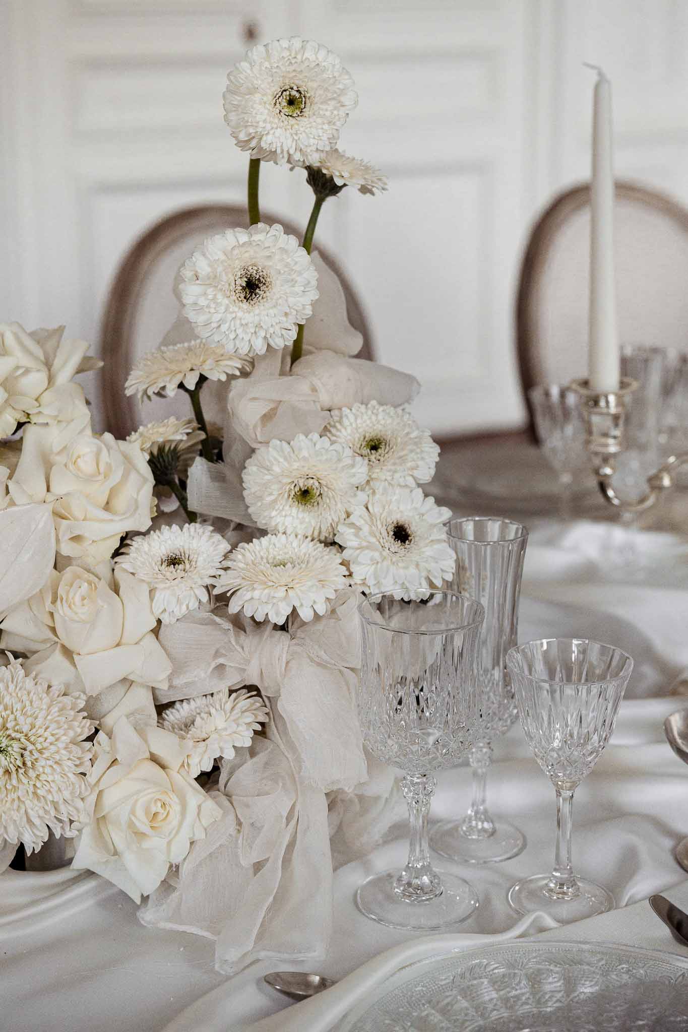 White gerbera daisy and cream rose centerpiece with crystal stemware on reception table