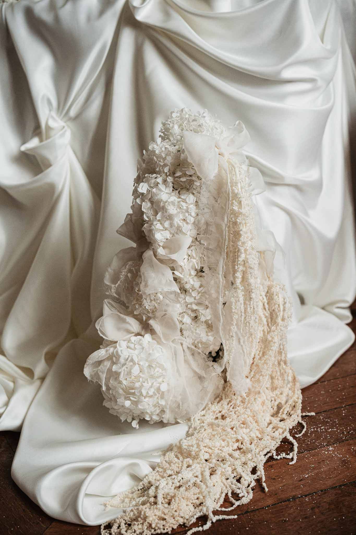 Wedding cake decorated with white hydrangeas and cream peonies with trailing lace veil on dark wood surface
