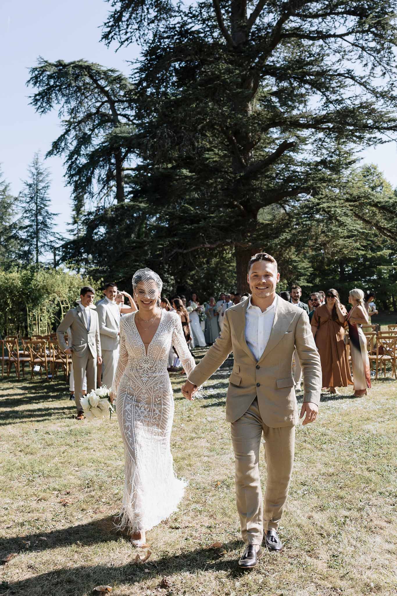 Bride and groom walking back up the aisle hand in hand as guests applaud at an outdoor garden ceremony