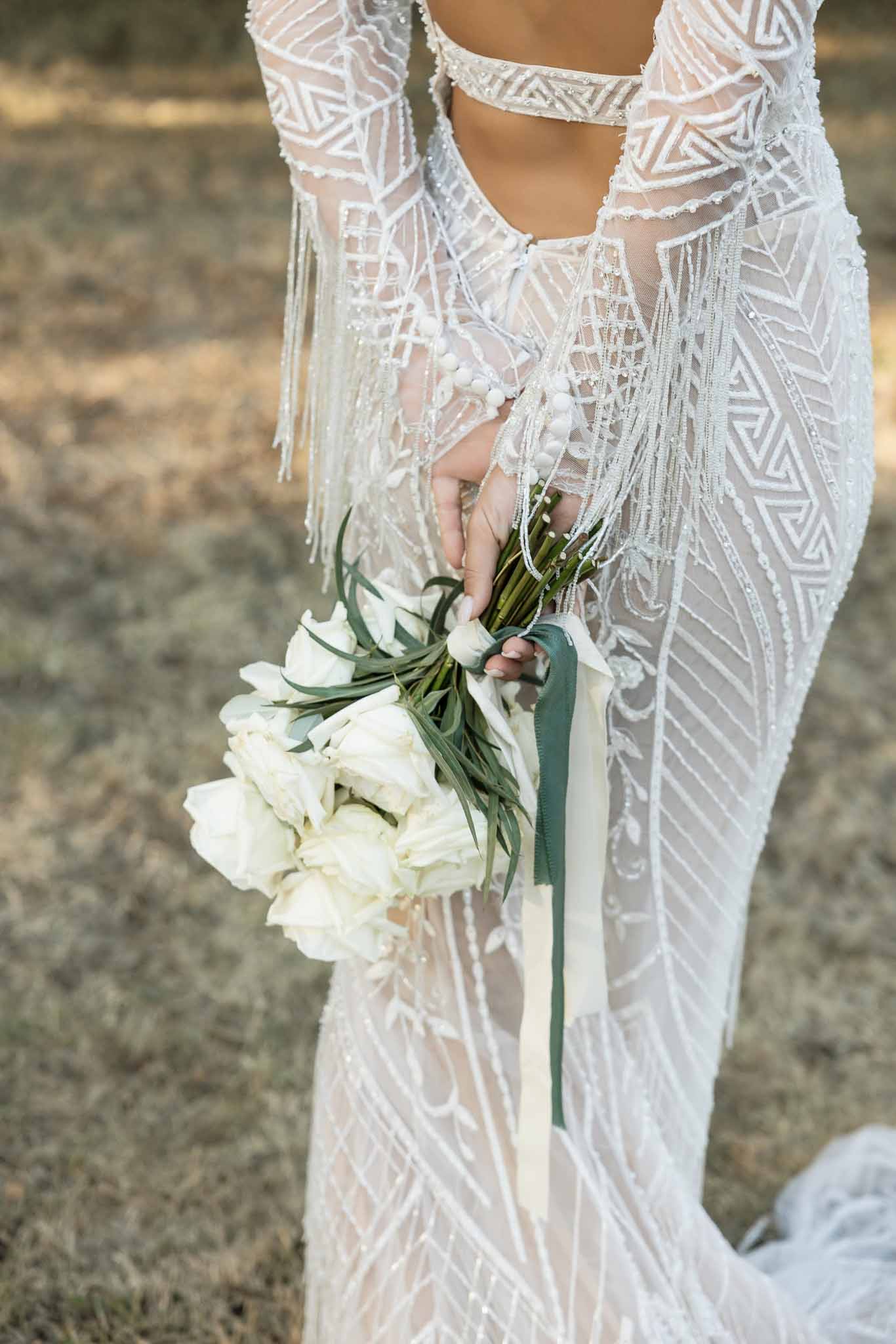 Close-up of bride's beaded Art Deco gown and white rose bouquet with sage green ribbons