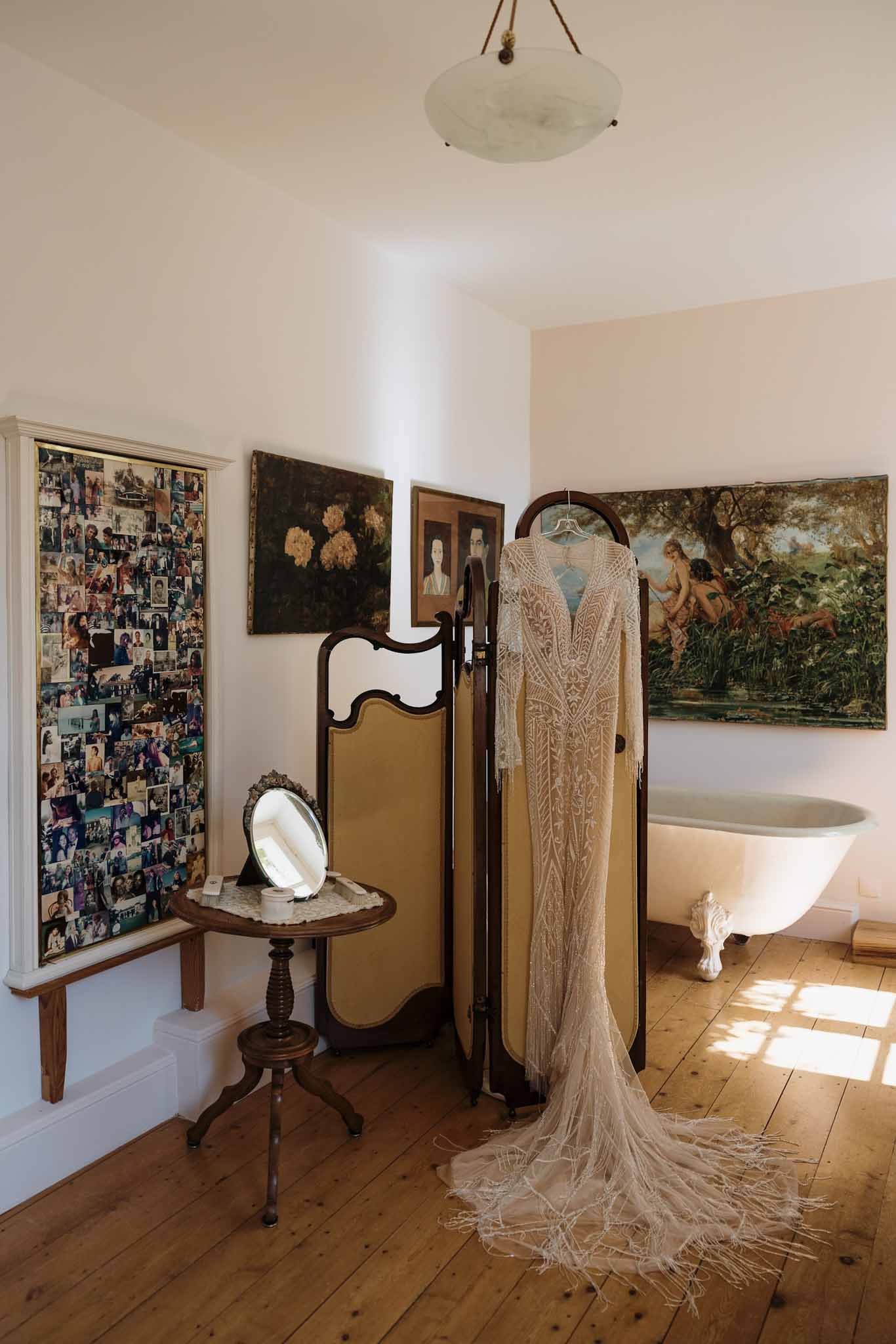 Embroidered lace wedding dress with fringed hem hung on folding screen in vintage room