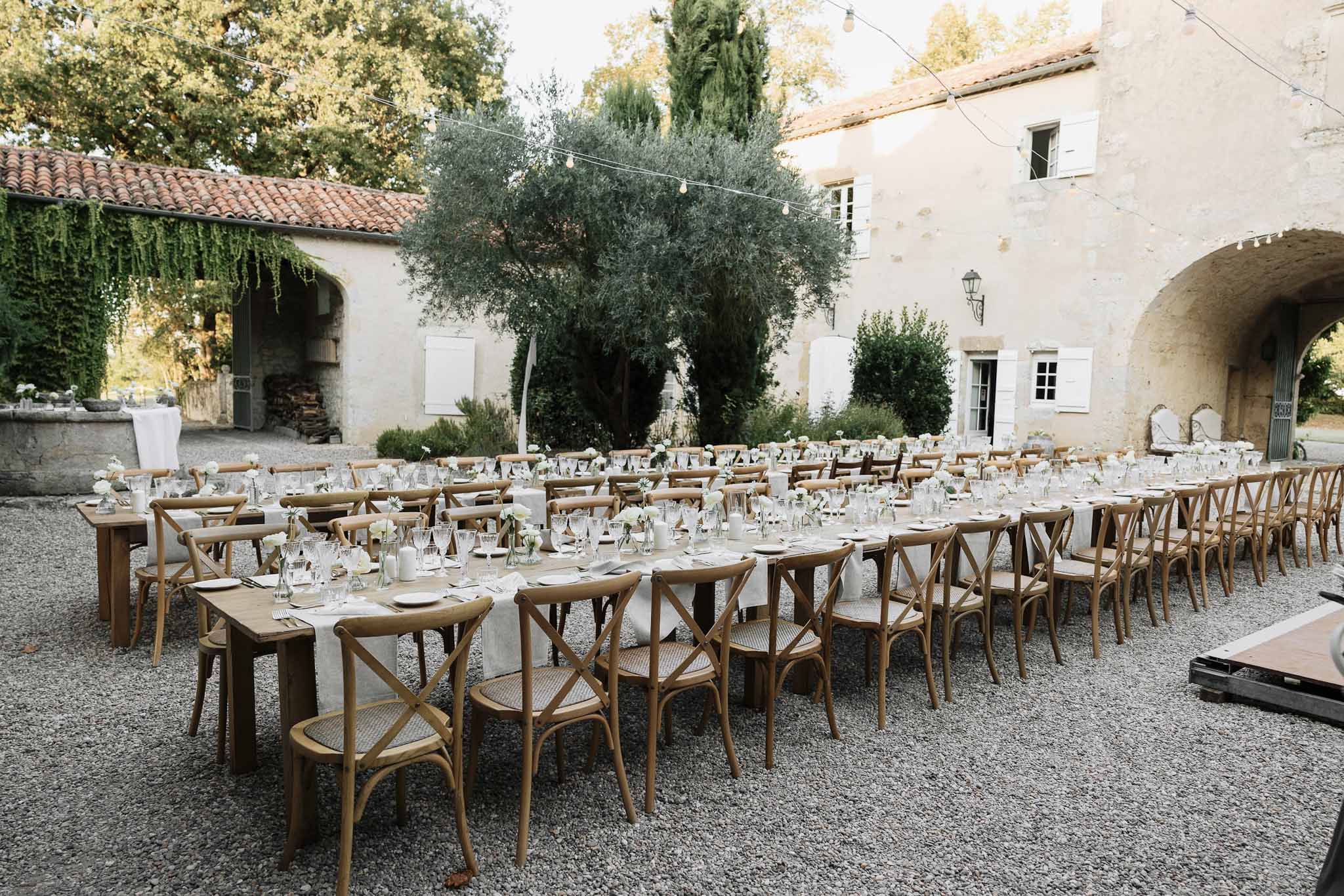 Provencal mas courtyard with wooden farm tables, cross-back chairs, white ranunculus, and globe lights