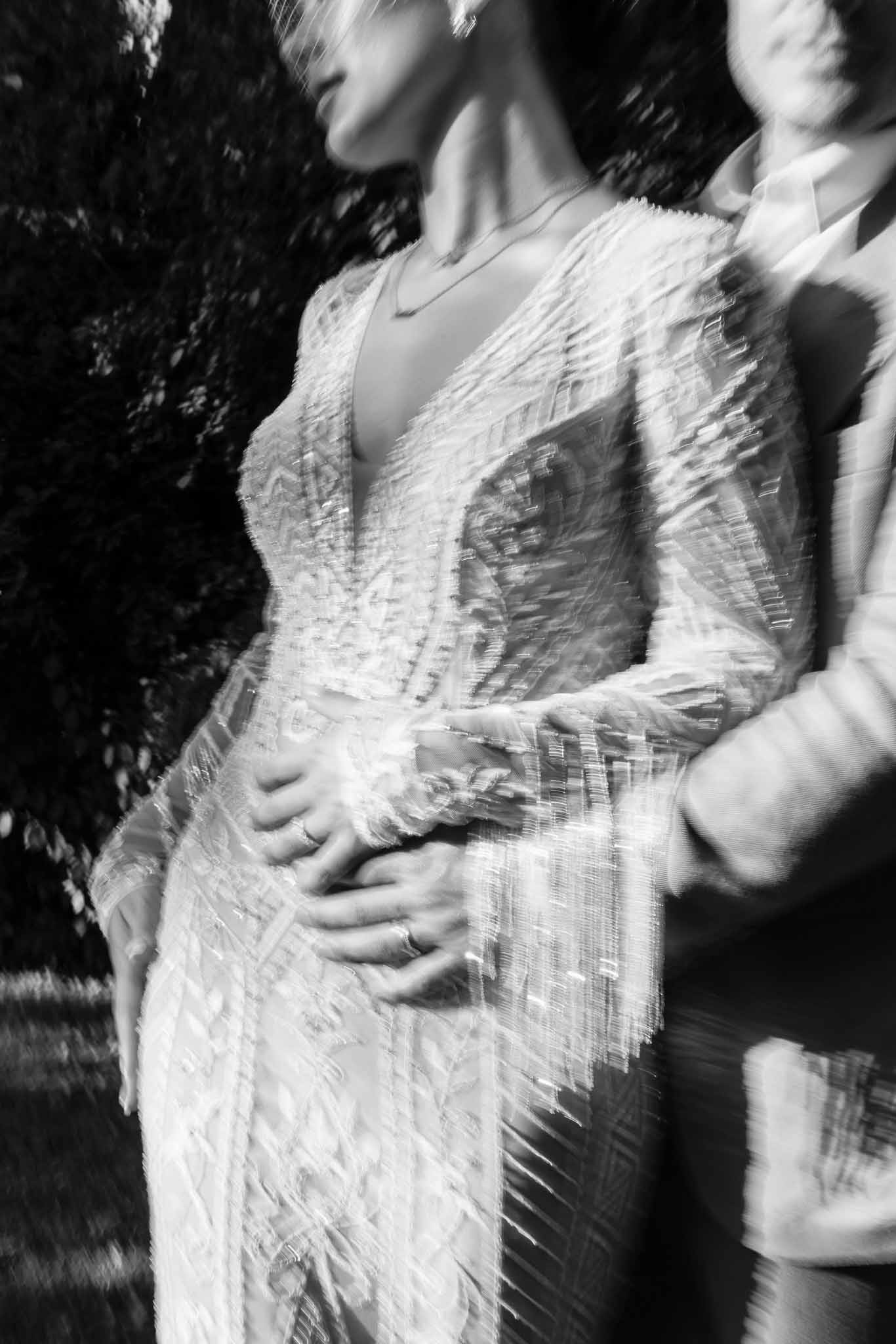 Black and white motion blur portrait of bride in beaded fringe dress and groom holding hands outdoors