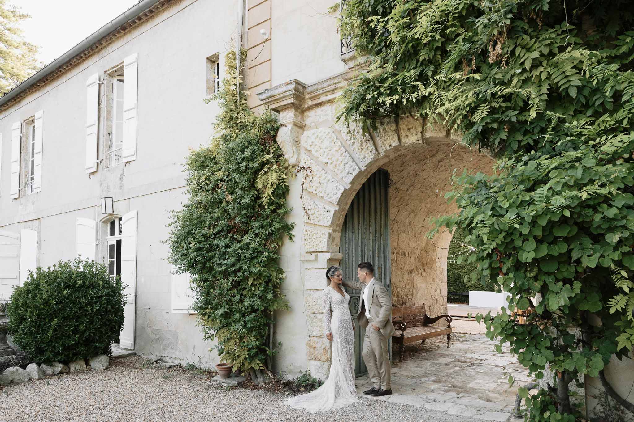 Couple facing each other under stone archway with teal door and climbing vines at French country estate