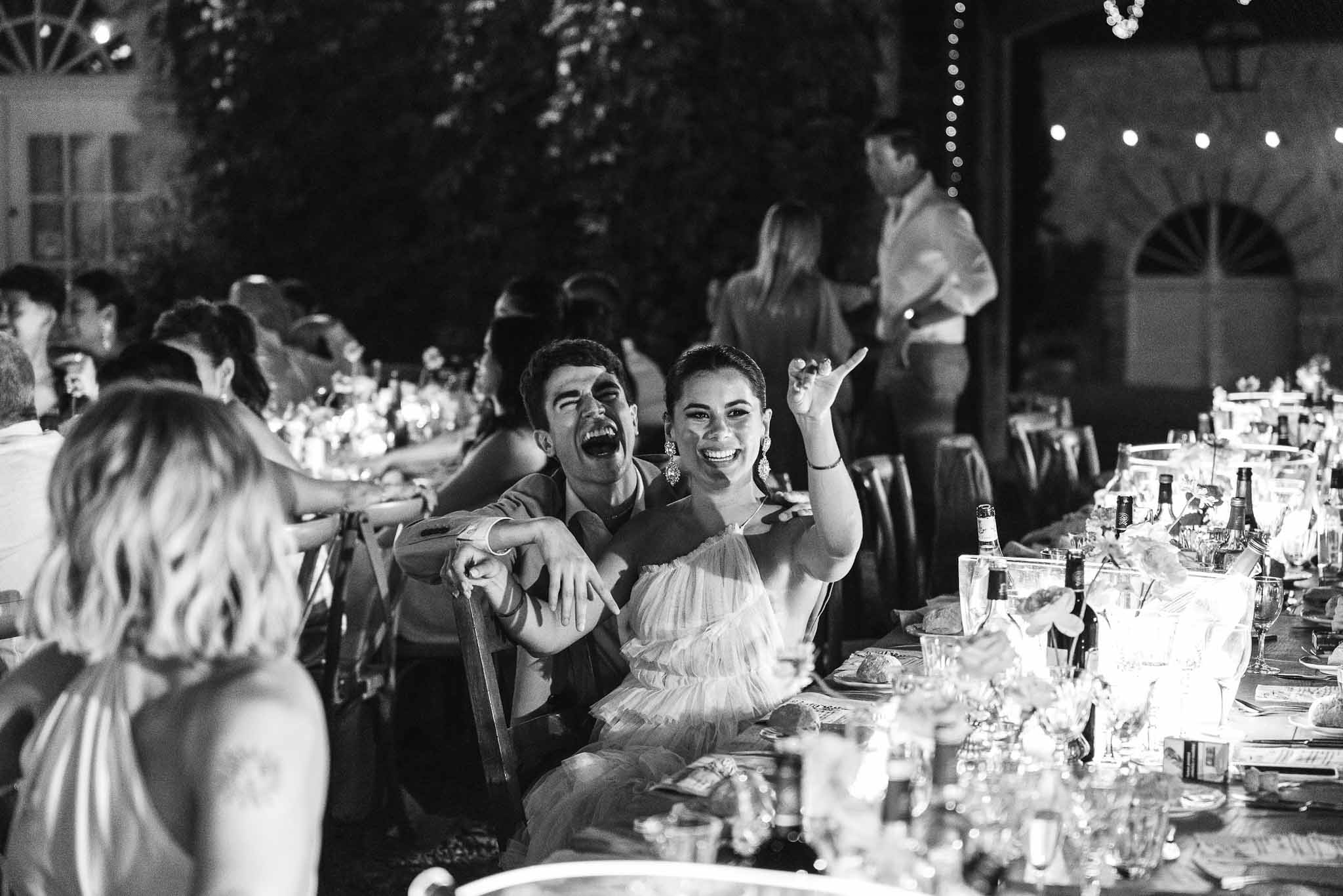 Black and white candid of laughing guests at outdoor evening reception under string lights