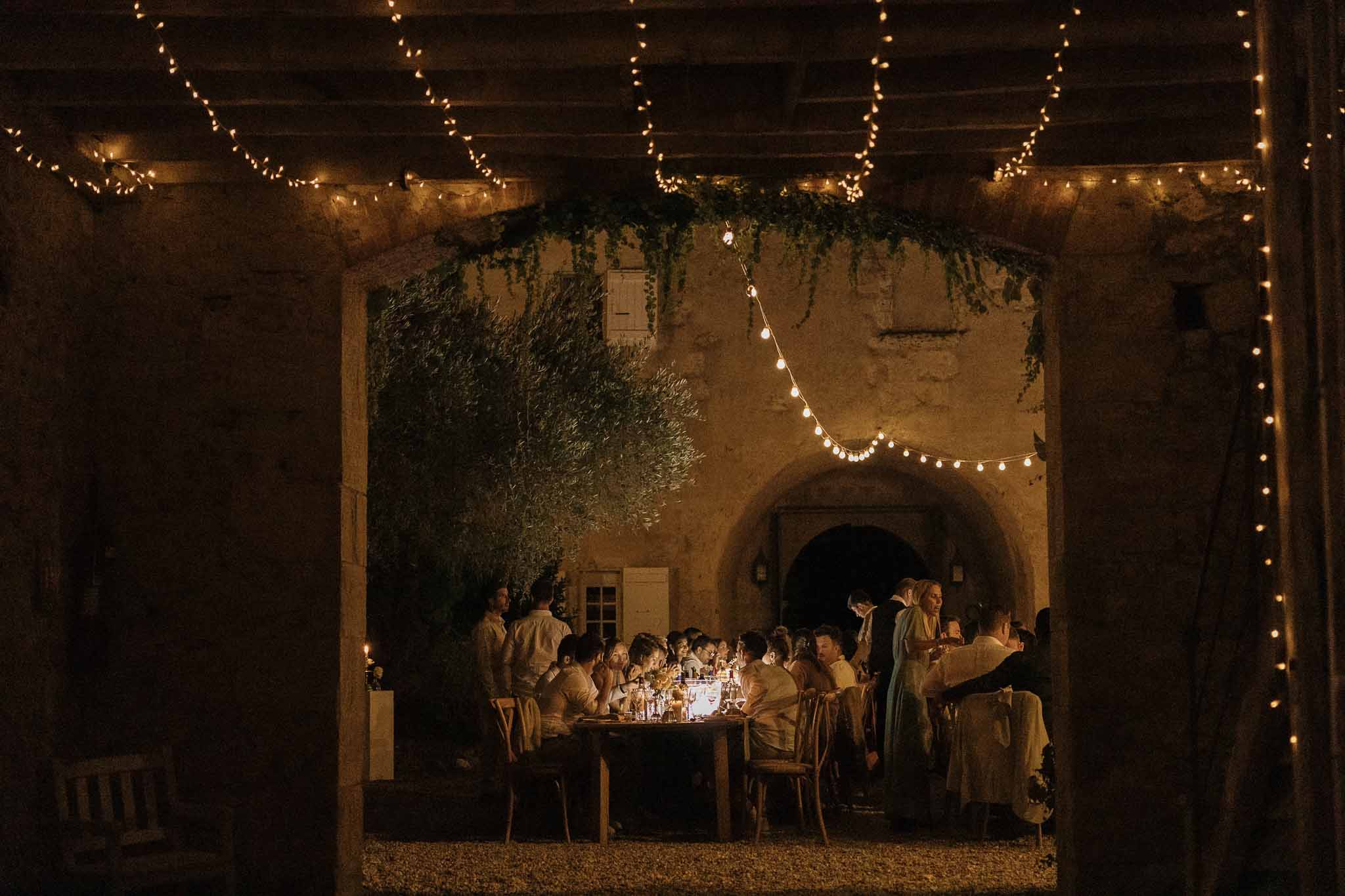 Candlelit courtyard dinner framed through stone archway with Edison fairy lights and climbing greenery