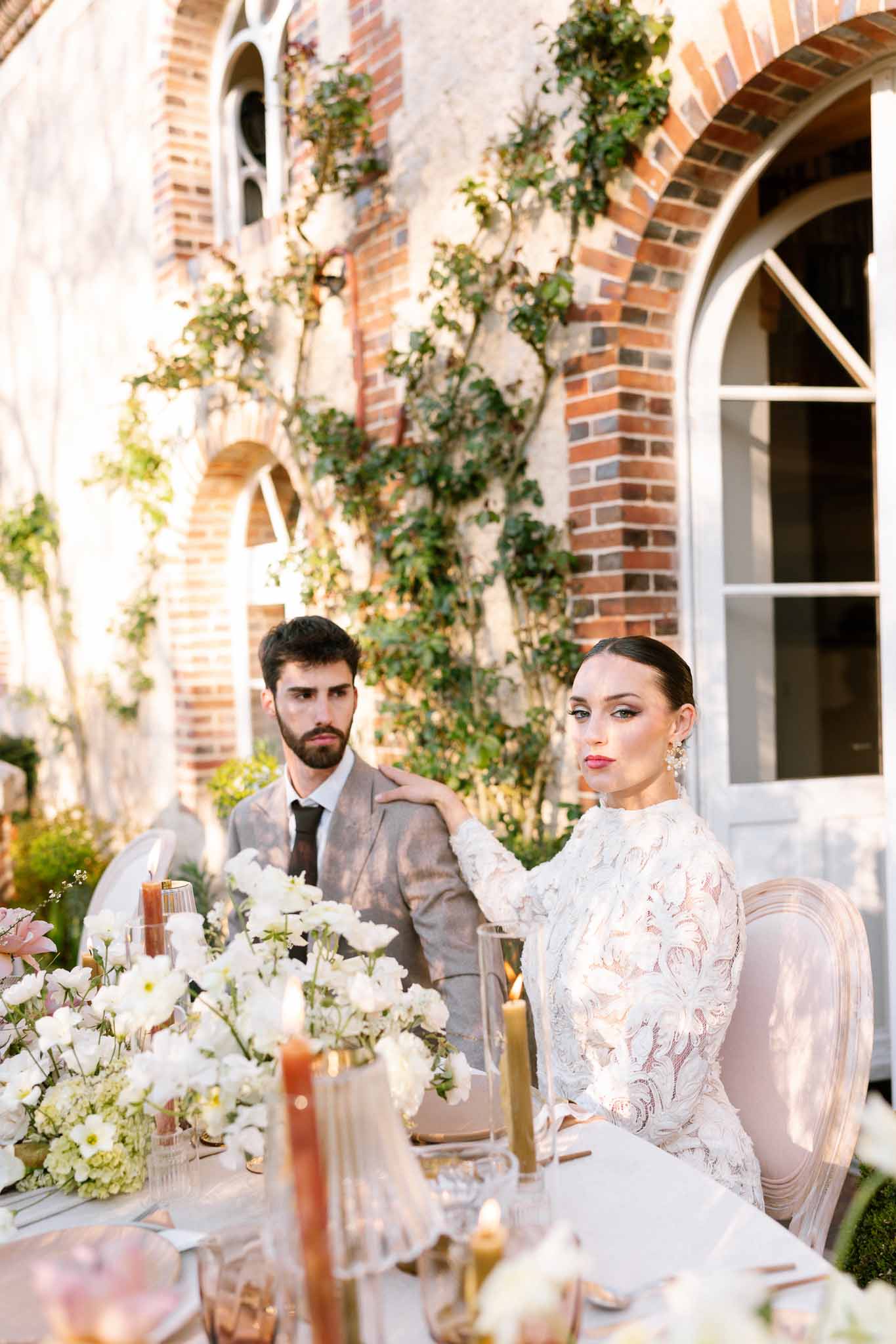 Bride and groom seated at outdoor reception table with floral centerpieces at historic brick venue