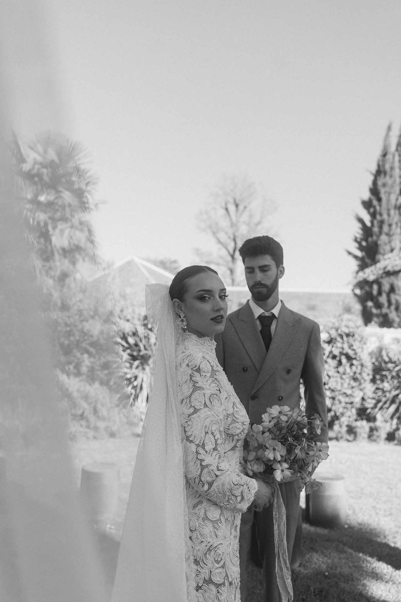 Bride and groom walking together down cypress-lined garden pathway at outdoor estate wedding venue