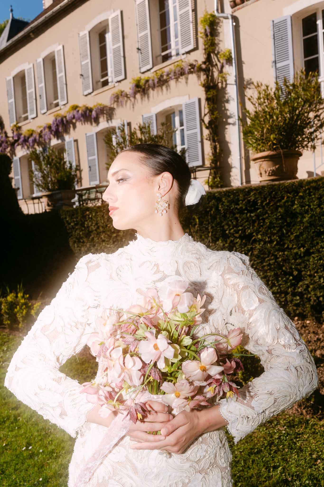 Bride in ivory lace dress holding pink and white bouquet at classical cream building with wisteria