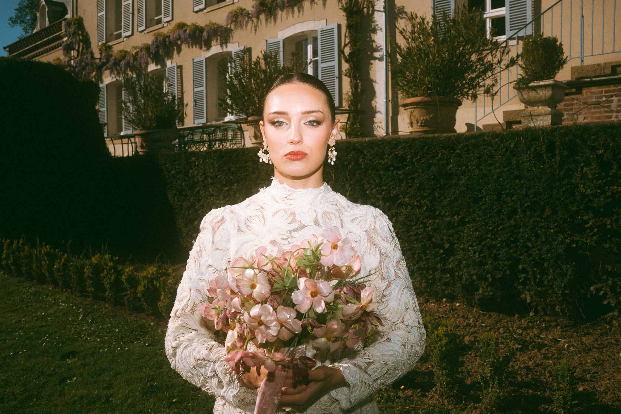 Bride in ivory lace gown holding dusty rose bouquet in European-style courtyard garden