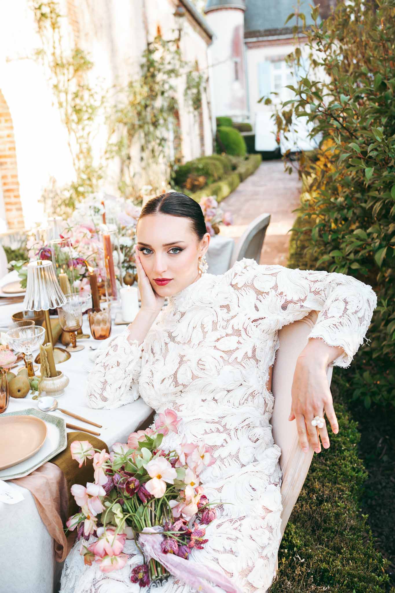 Bride in ivory lace dress posing at decorated reception table in ivy-covered courtyard