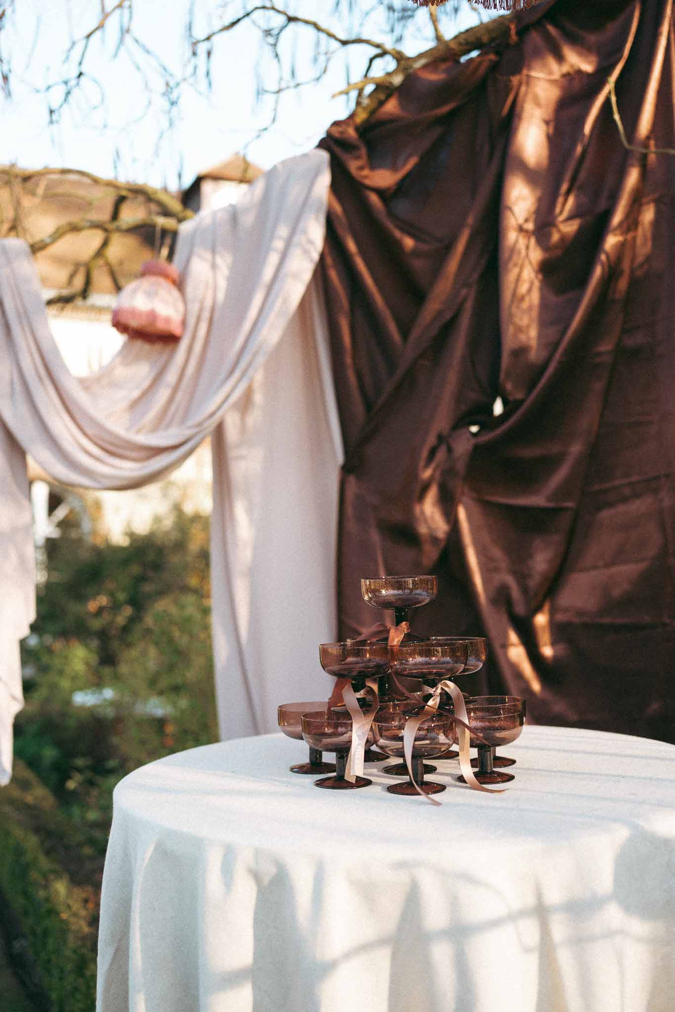 Tiered champagne tower with rose-gold framework at outdoor cocktail hour setup in garden courtyard