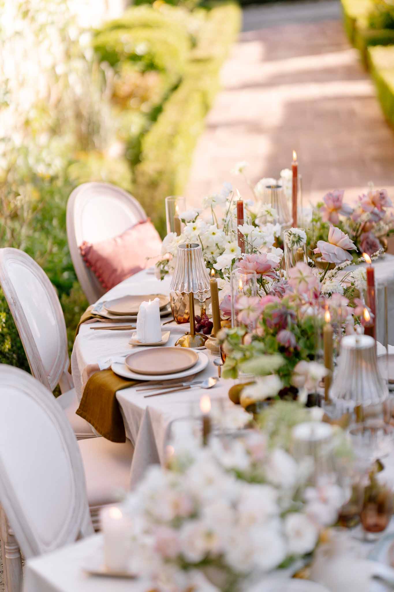 Long banquet table with white linens and floral centerpieces at outdoor garden wedding reception