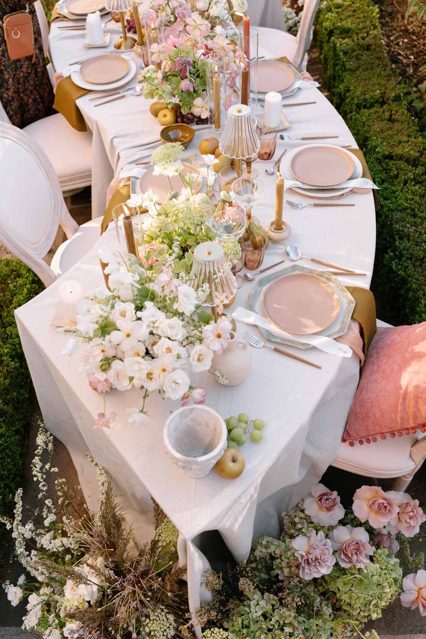 Overhead view of elegant reception table with blush chargers and rose gold flatware in garden setting