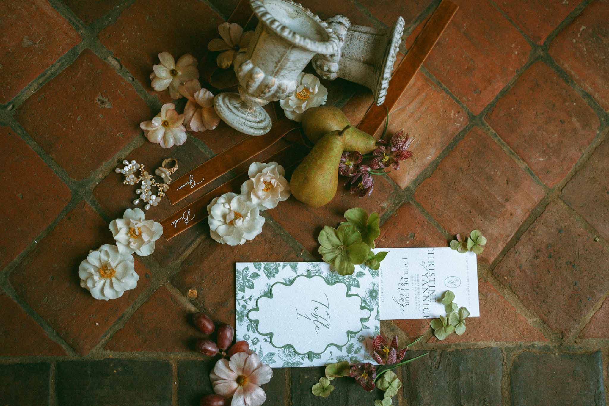 Wedding stationery flat lay with cream roses and burgundy florals on terracotta brick floor