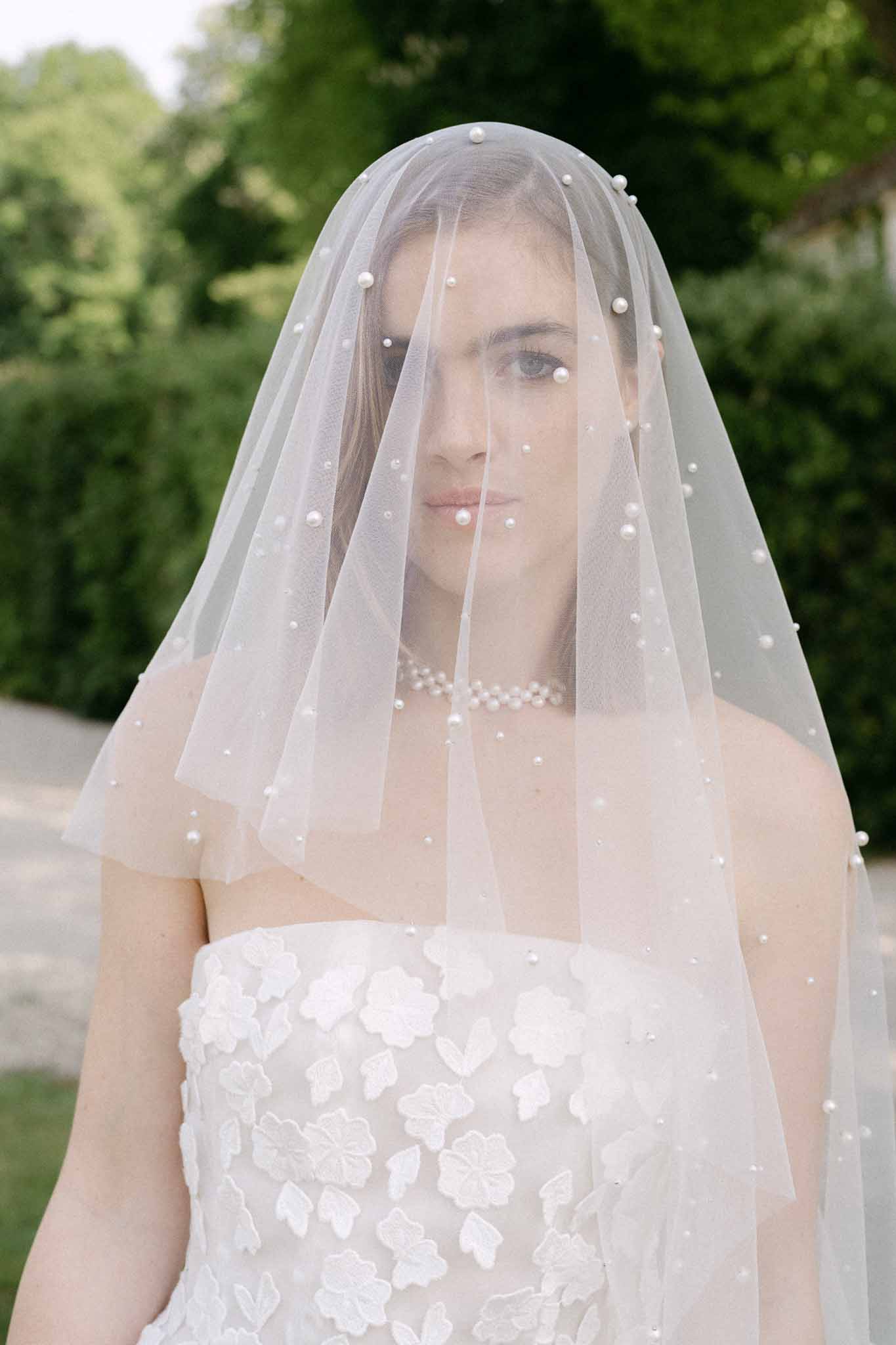Bride in ivory strapless gown with floral appliqués and beaded veil in garden setting
