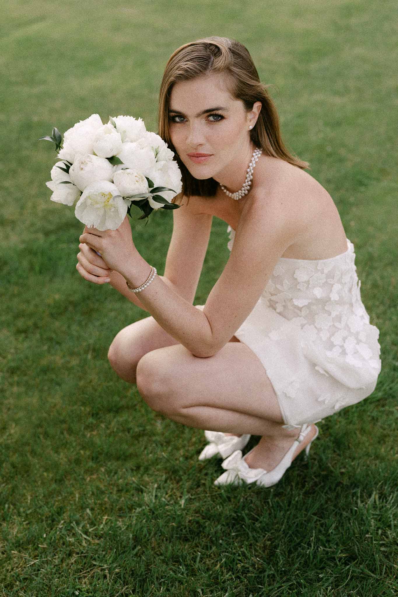 Bride in white dress holding peony bouquet in outdoor garden portrait