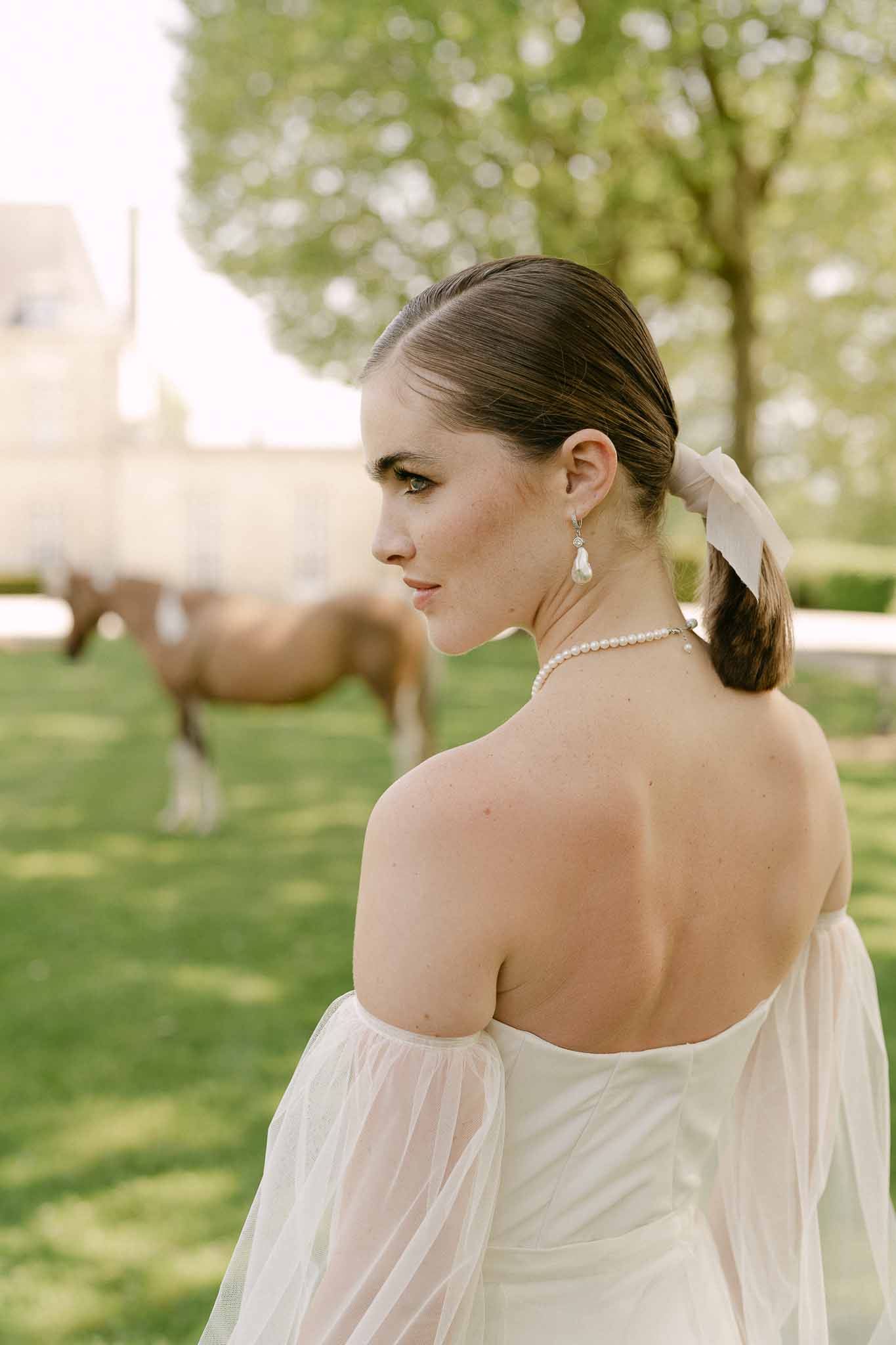 Bride in ivory strapless gown with pearl accessories standing in garden with white blossoms