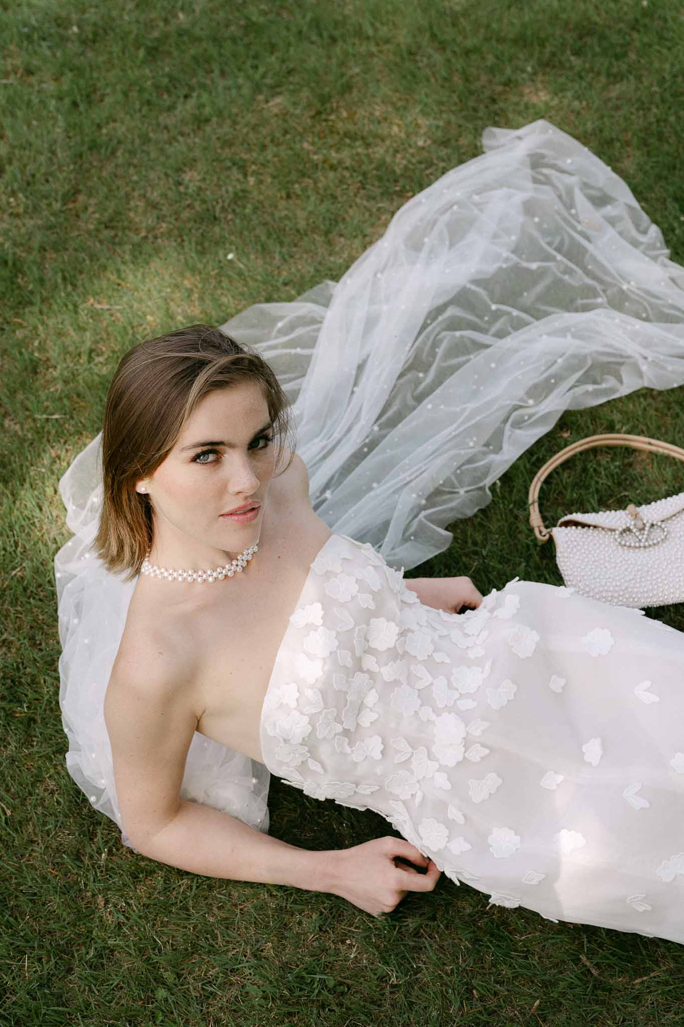 Bride in ivory wedding dress with floral appliqués lying on grass in aerial portrait shot