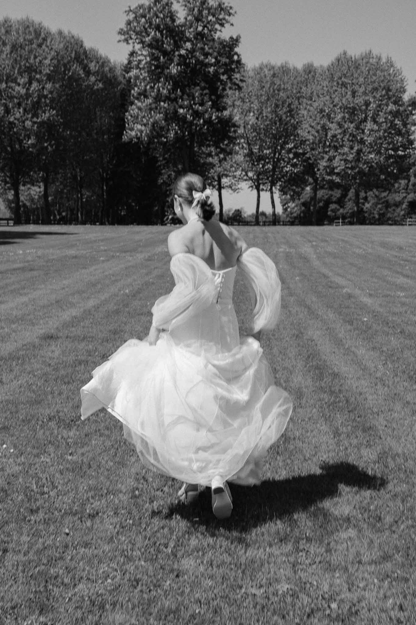 Bride walking in flowing wedding gown in open field with trees