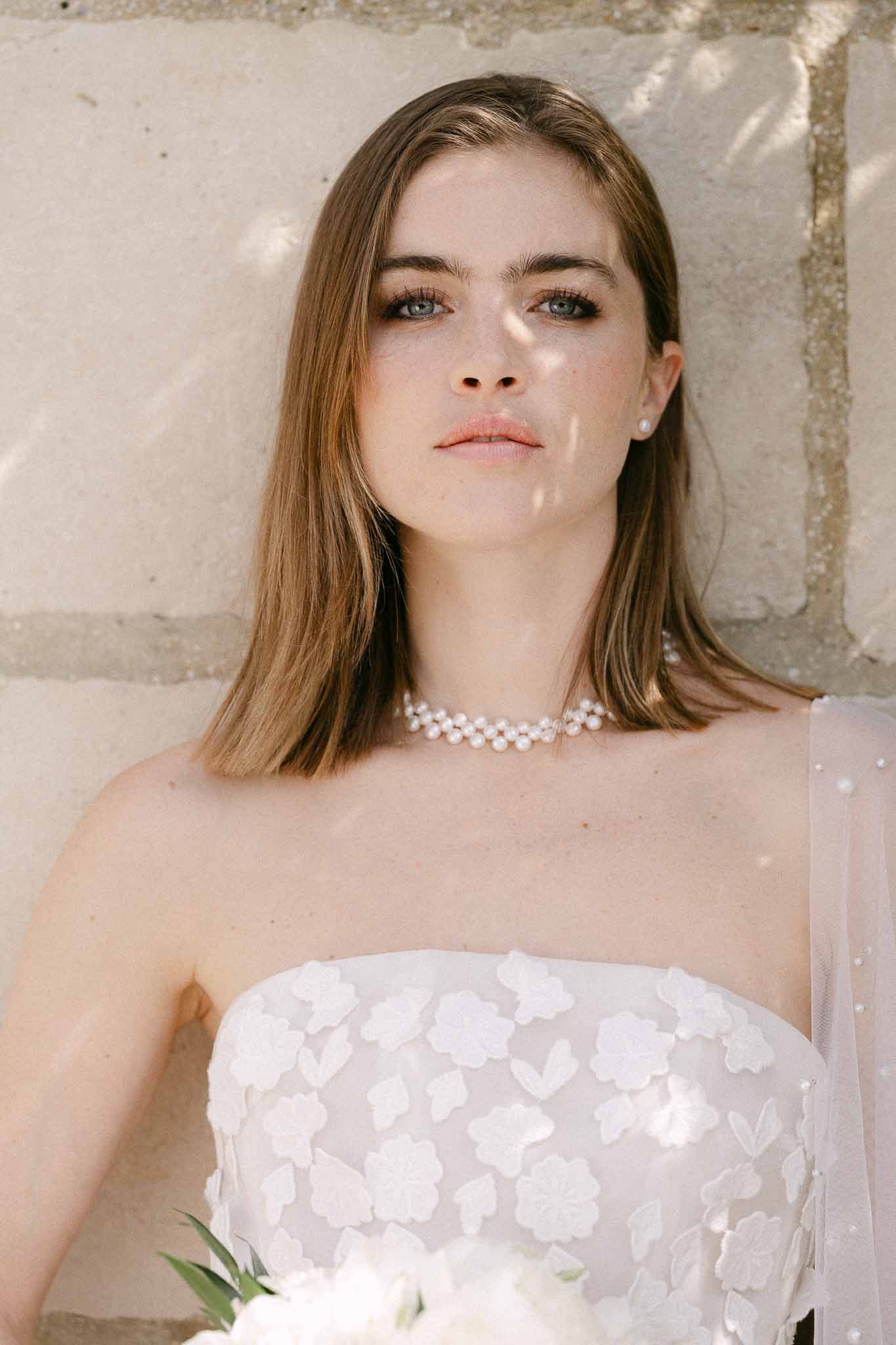 Bride in ivory strapless wedding dress with floral appliqués against stone wall
