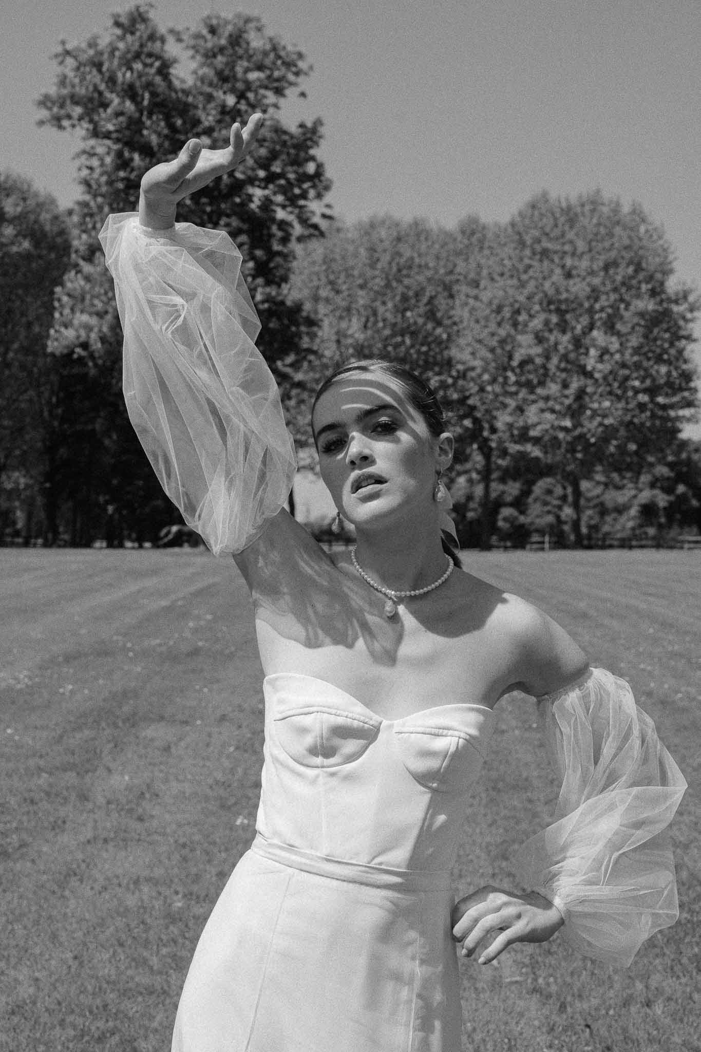 Bride in strapless wedding dress with tulle cape posing in field with trees