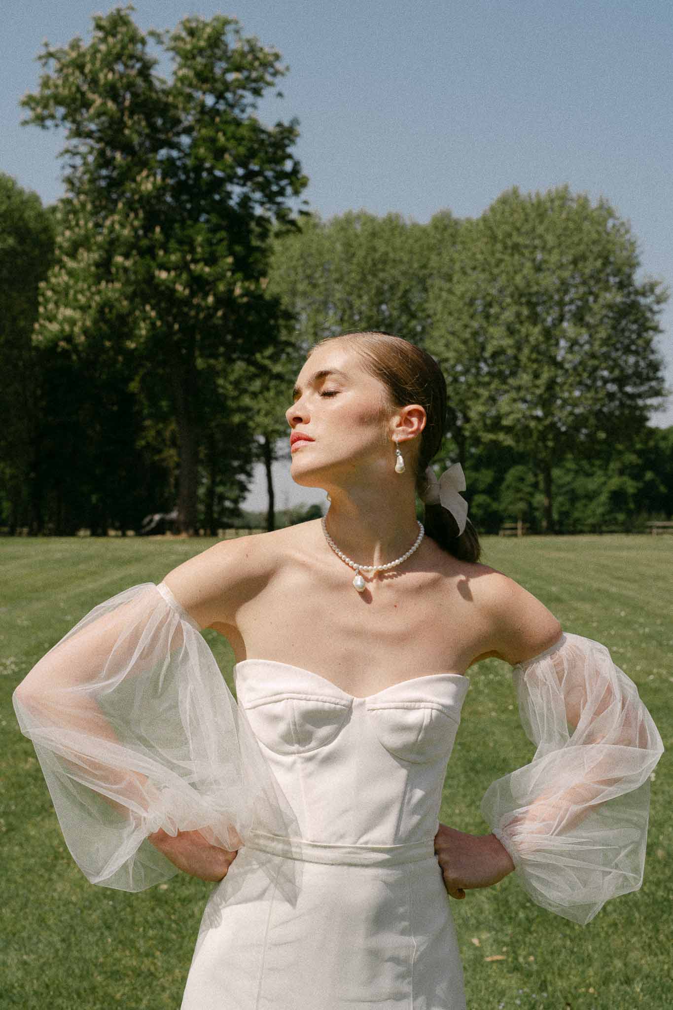 Bride in ivory strapless gown with tulle sleeves posed in manicured garden setting