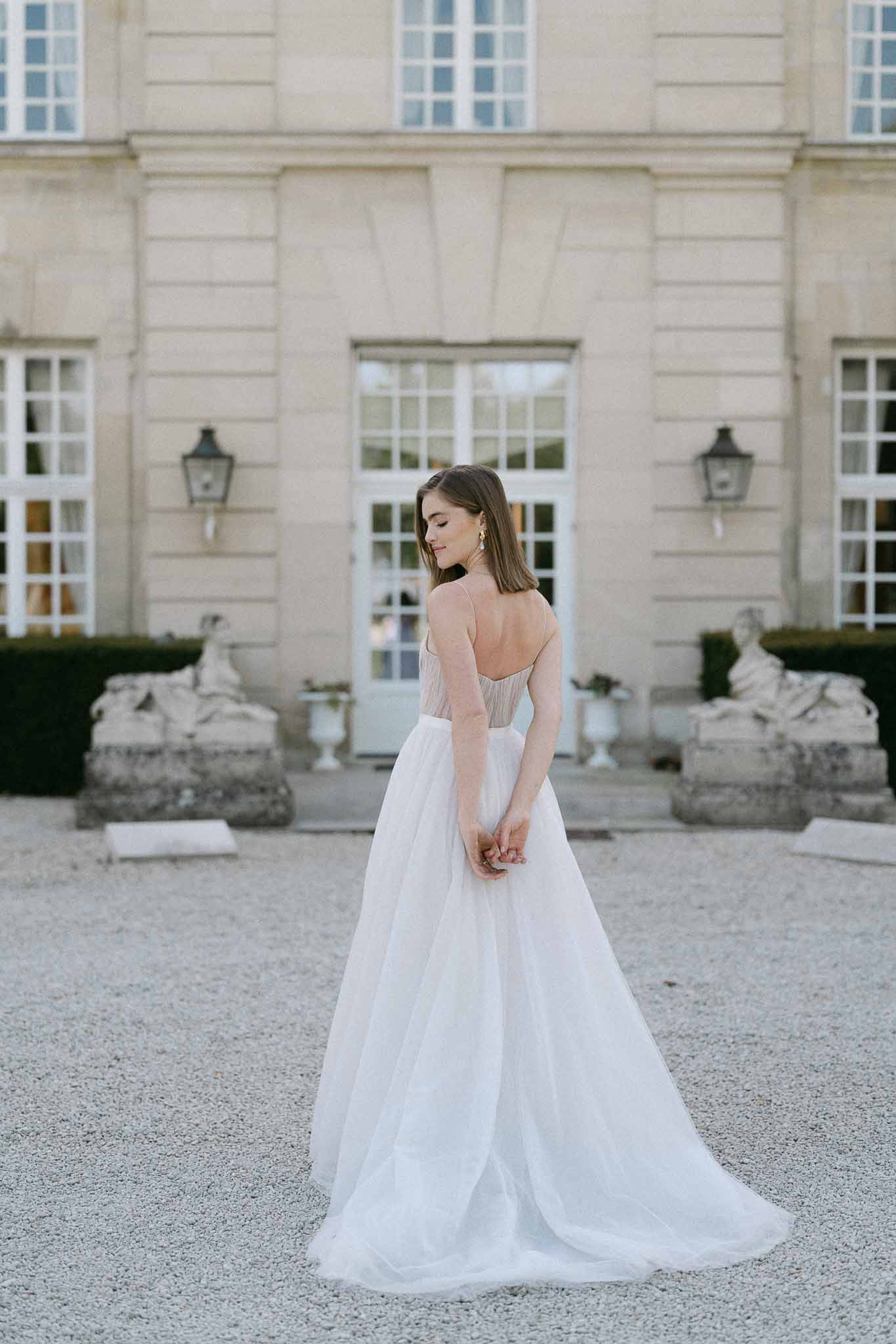 Bride in blush and ivory wedding ensemble standing in courtyard of neoclassical stone building