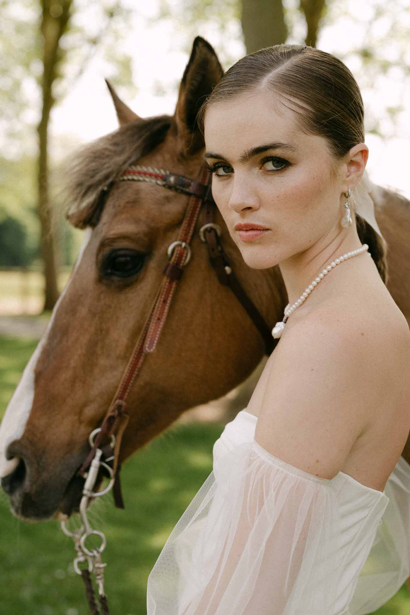 Bride in ivory strapless dress posing with chestnut horse in garden setting